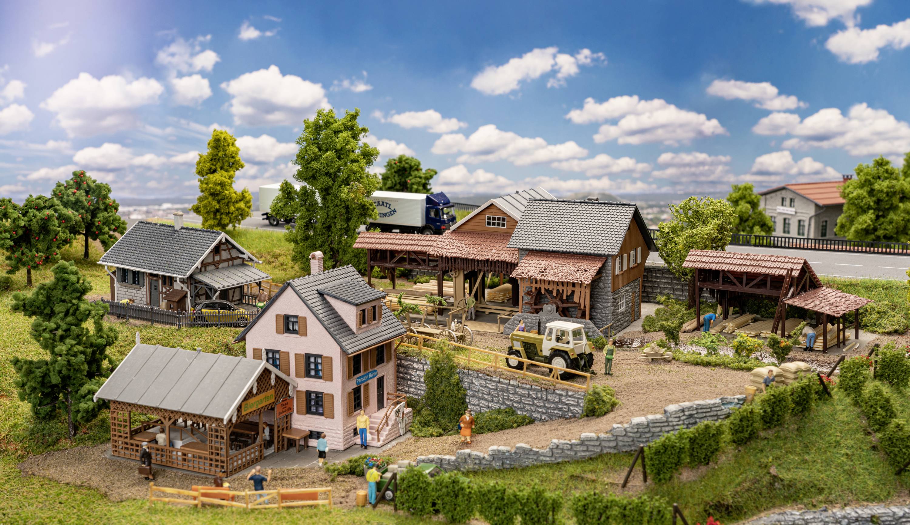 Eine idyllische Modelleisenbahnlandschaft mit Bauernhofgebäuden, Traktoren und grasbewachsenen Hügeln unter einem blauen Himmel mit Wolken.