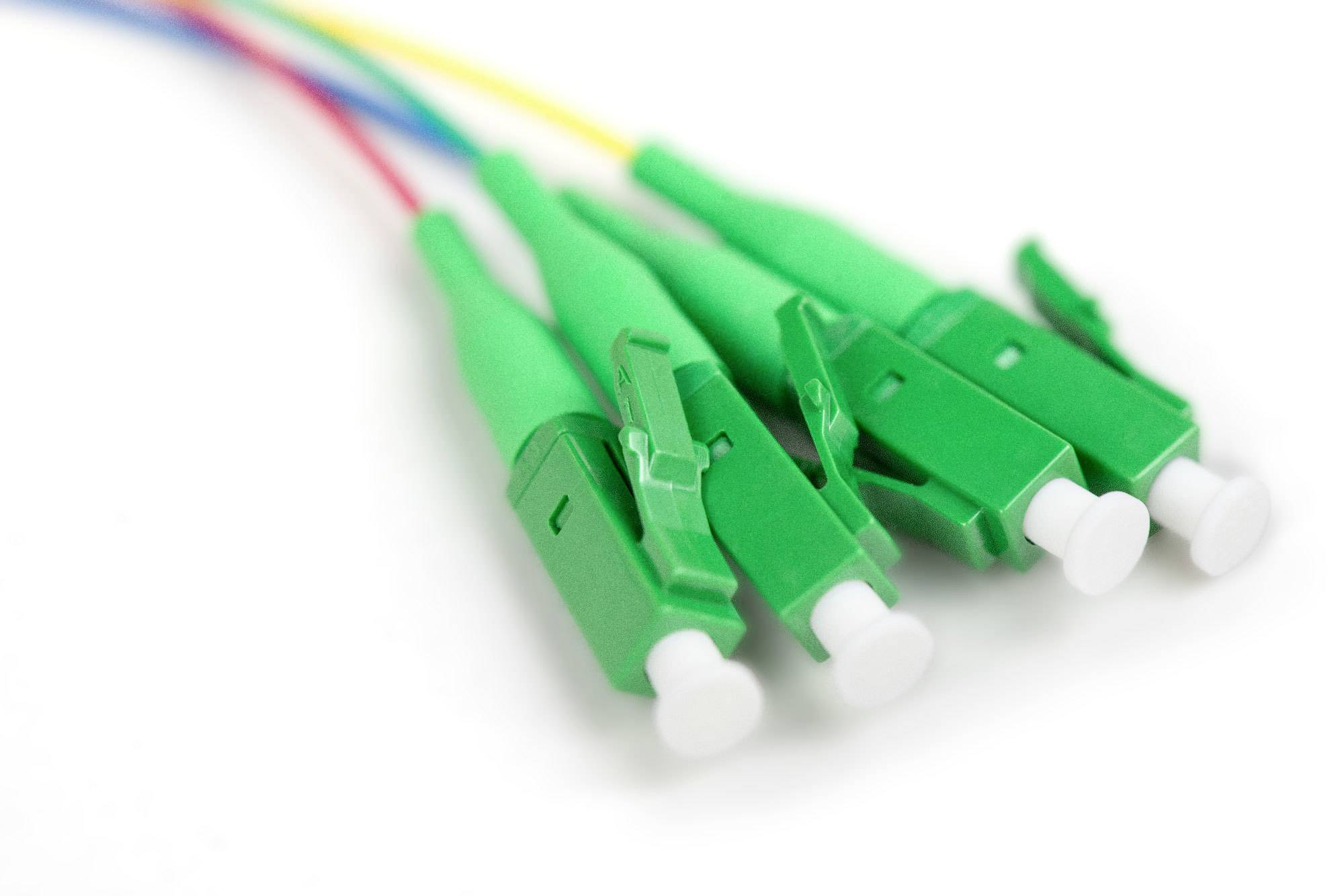 Vier grüne Glasfaserkabelstecker auf weißem Hintergrund. Die Stecker sind in einer Linie angeordnet und mit bunten Kabeln verbunden.