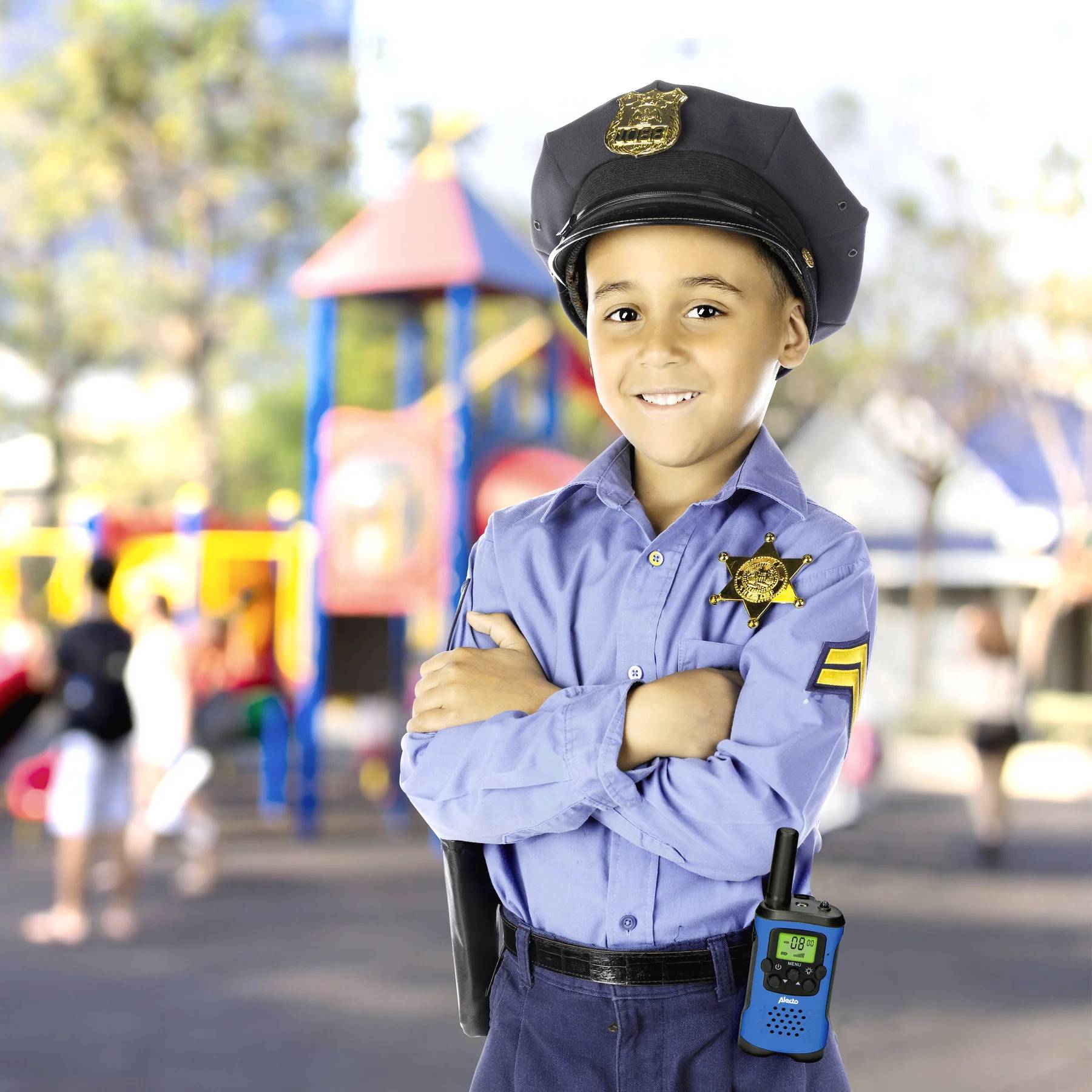 Ein Kind in einem Polizeikostüm steht auf einem Spielplatz und lächelt in die Kamera. Im Hintergrund sind Spielgeräte und andere Kinder zu sehen.