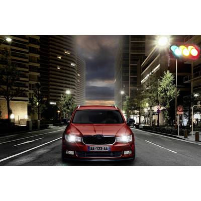 Rotes Auto fährt bei Nacht durch eine beleuchtete Stadtstraße, hält an einer Ampel mit roten, gelben und grünen Lichtern.