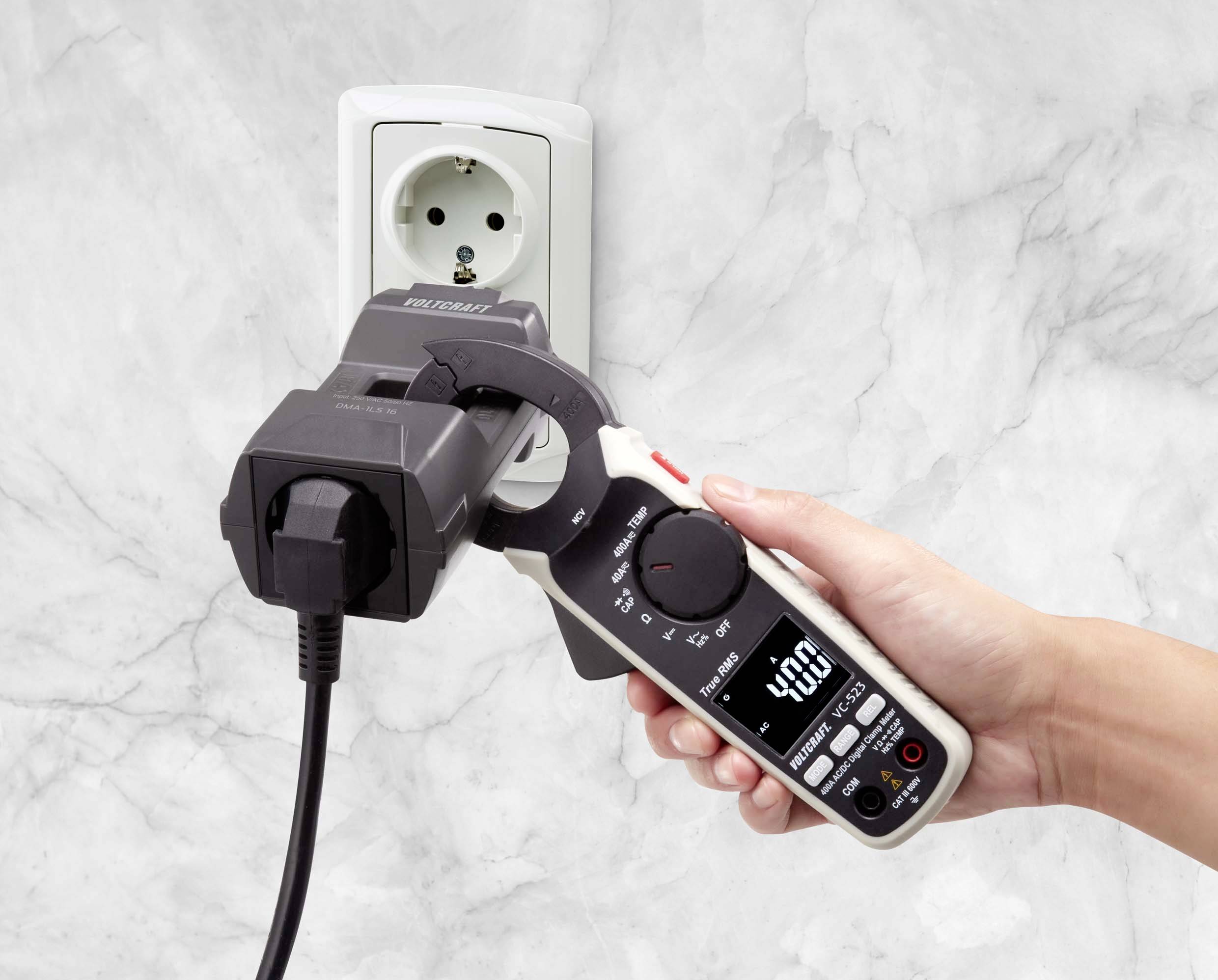 Eine Hand hält ein digitales Strommessgerät, das an eine Steckdose mit eingestecktem Gerät angeschlossen ist und 230,0 Volt anzeigt.