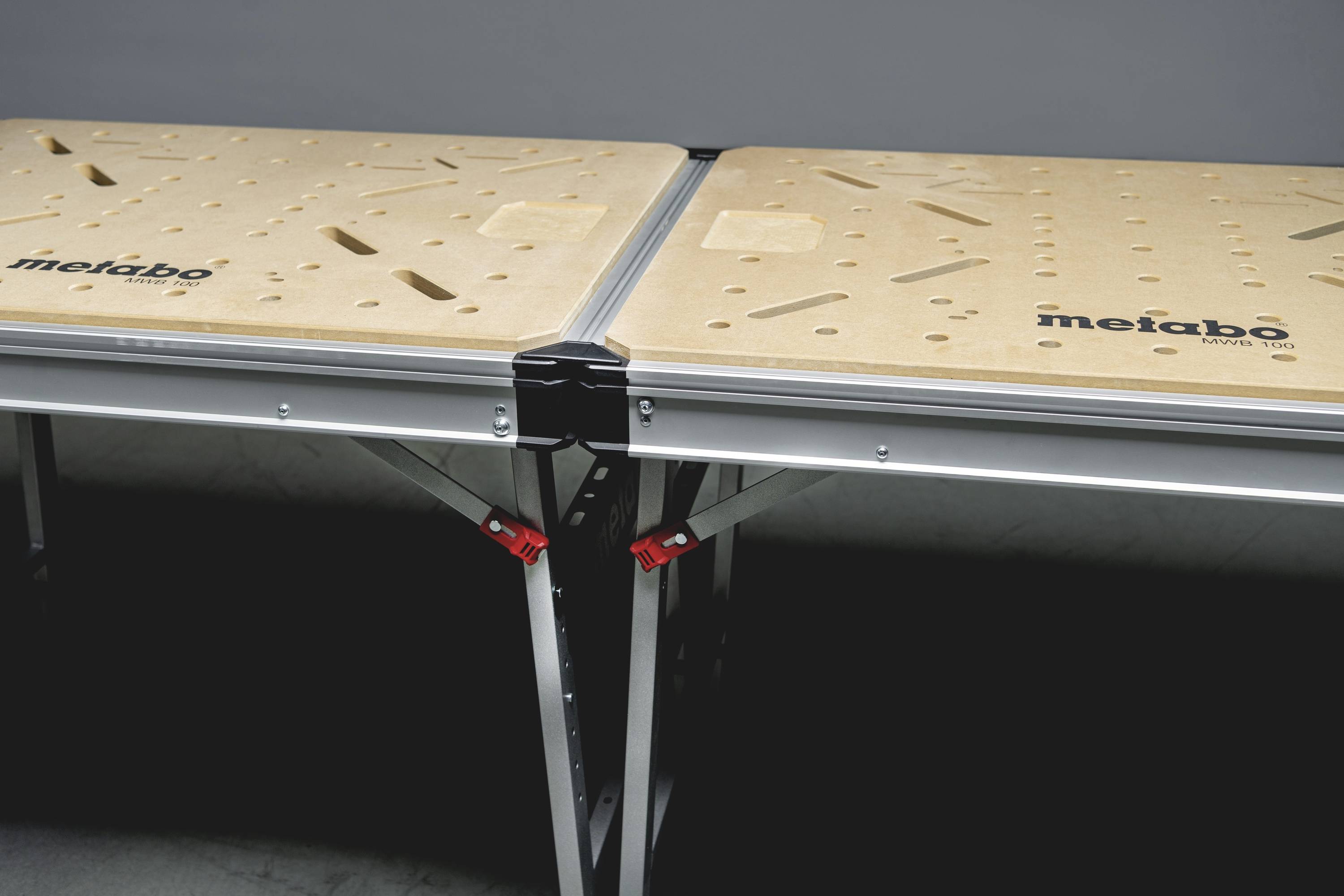 Ein zusammenklappbarer Arbeitstisch mit zwei Holzplatten und Metallo-Beinen, geeignet für handwerkliche oder industrielle Arbeiten.