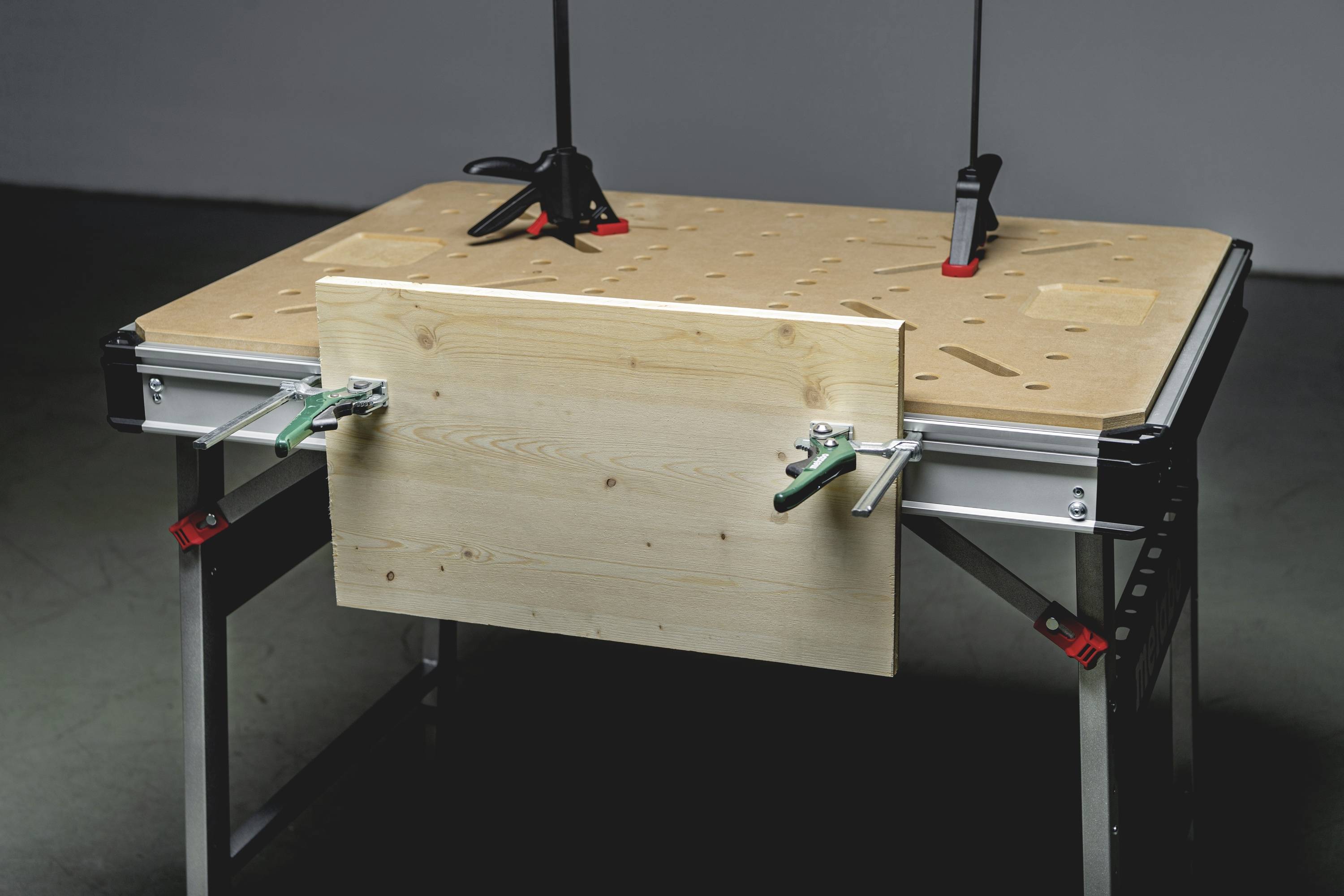 Ein Holztisch mit Metallbeinen und verschiedenen Klemmen, geeignet für handwerkliche Arbeiten oder als Werkbank.