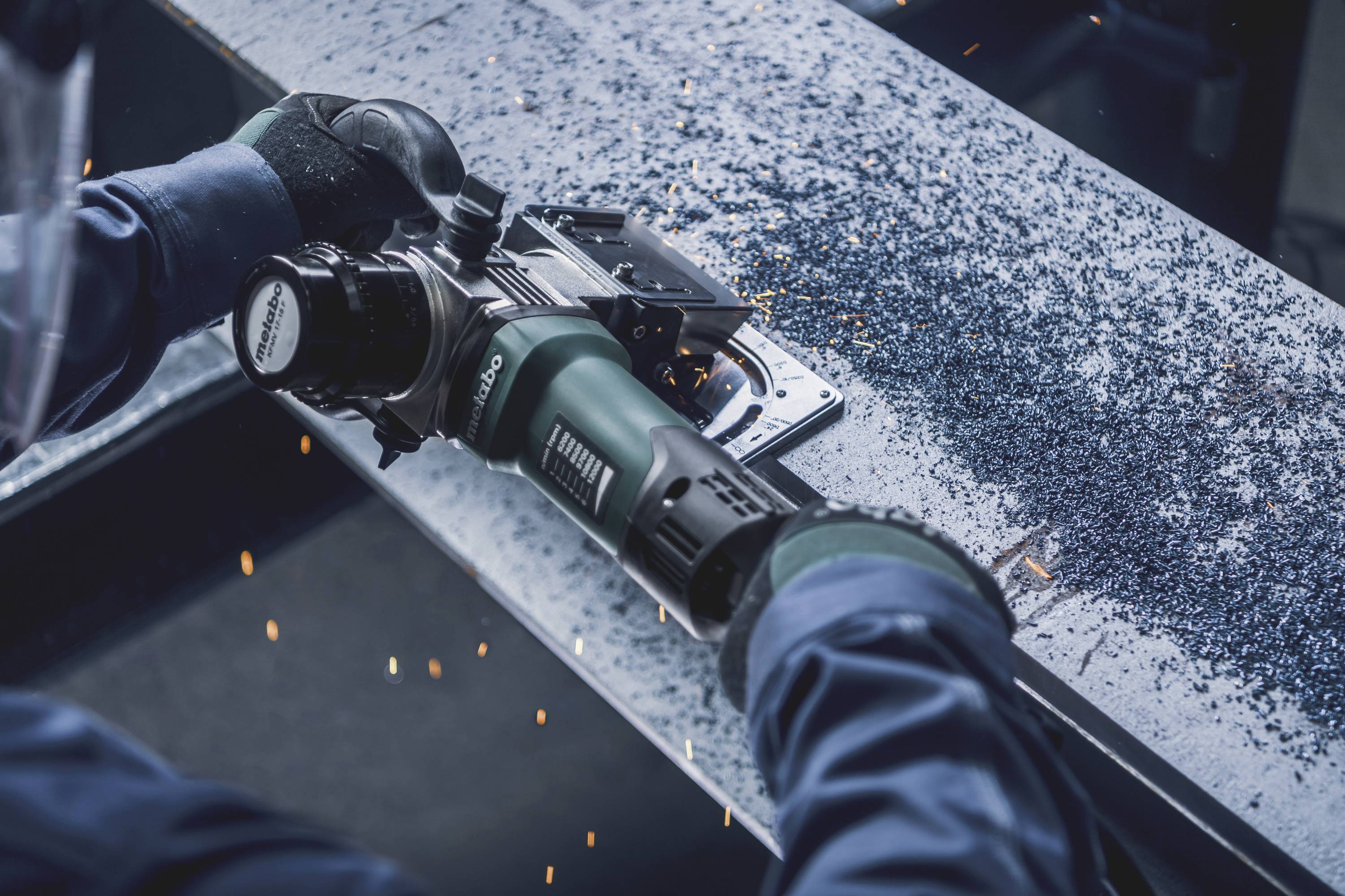 Eine Person arbeitet mit einer Schleifmaschine auf einem metallischen Werkstück, funkelnde Partikel fliegen umher.