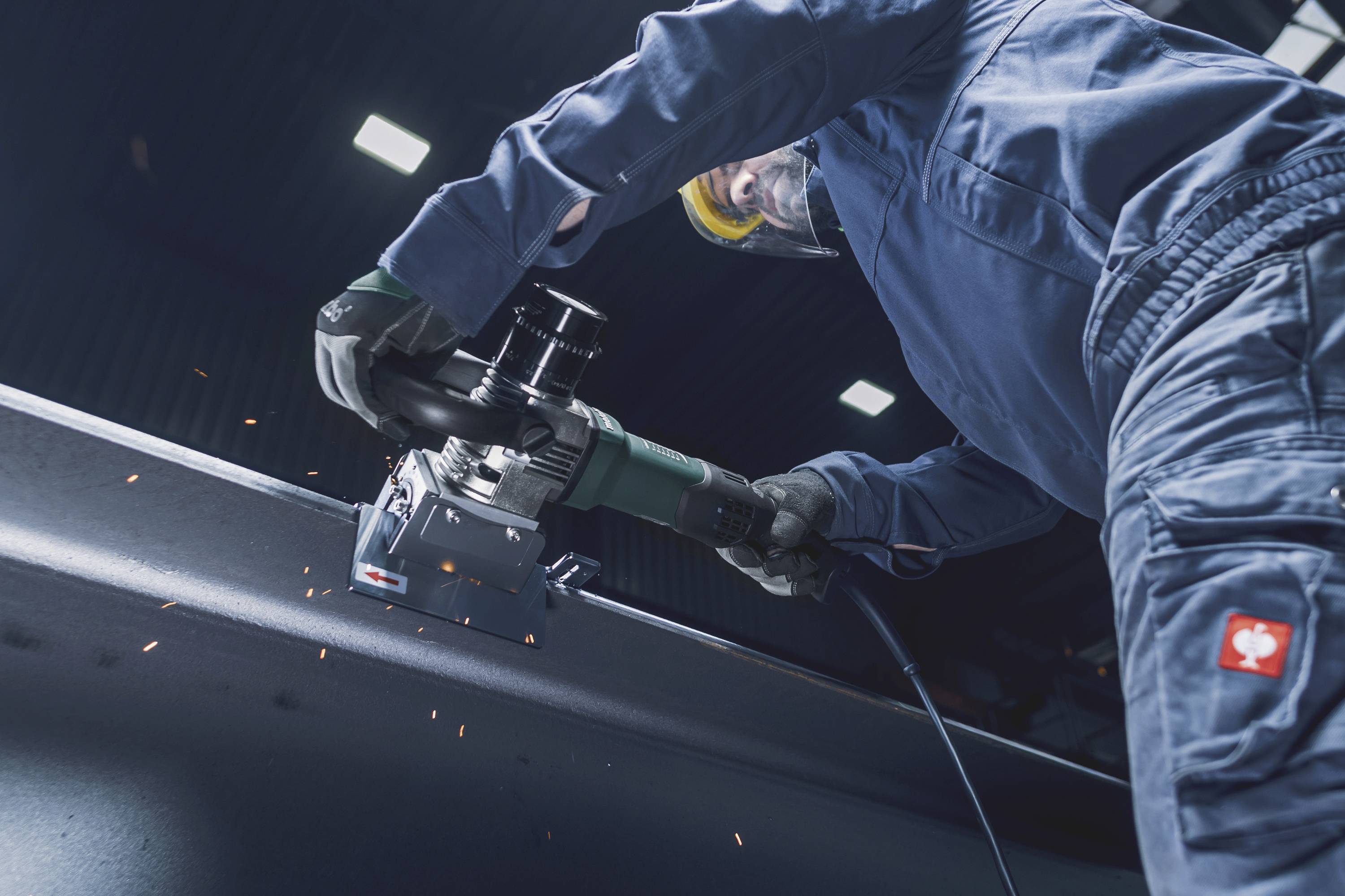 Eine Person in Schutzkleidung schleift mit einem Elektrowerkzeug Metall. Funken fliegen während der Arbeit in einer Werkstatt.