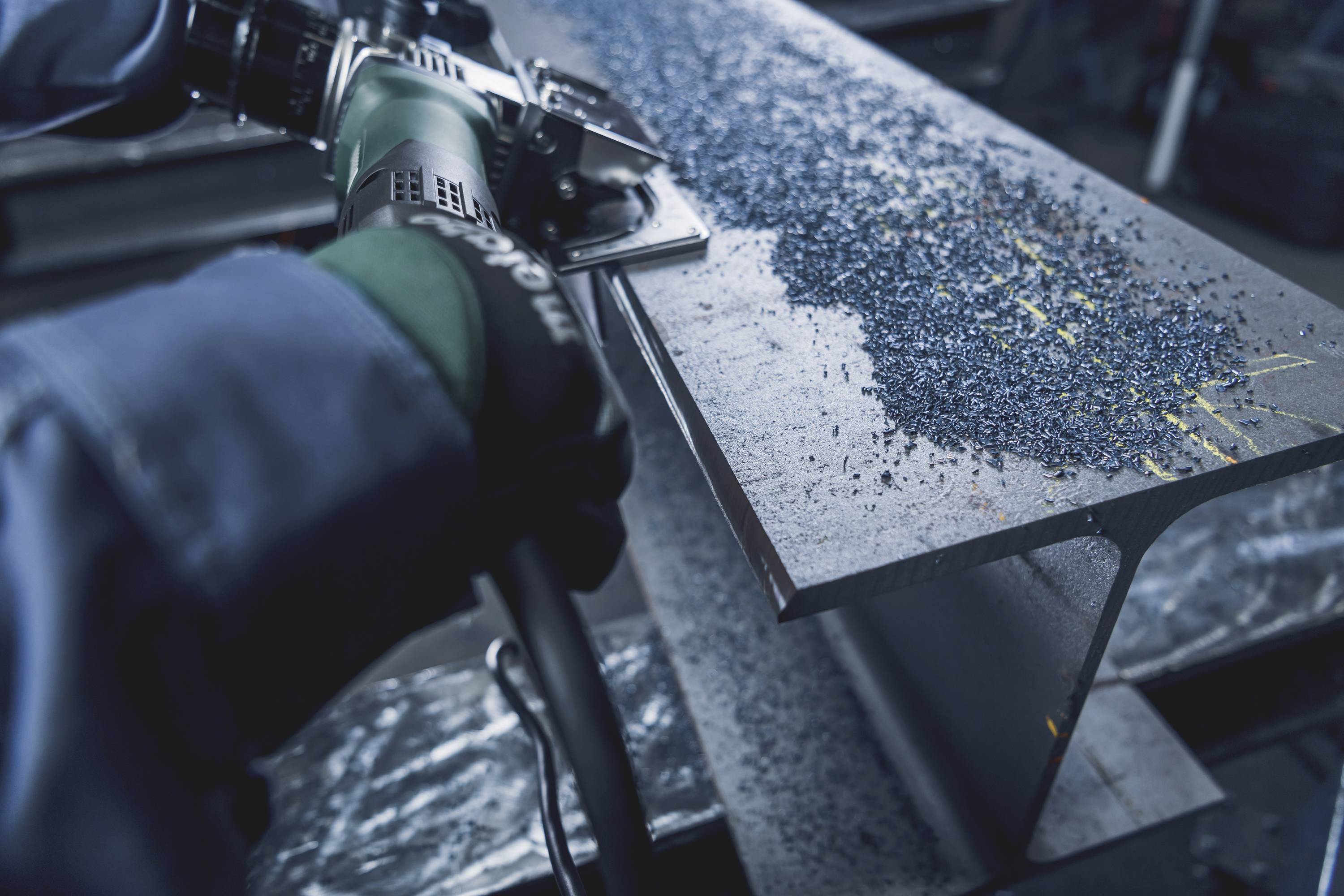 Arbeiter verwendet ein Schleifgerät, um Metallspäne von einem großen I-Träger zu entfernen. Konzentration auf präzise Bearbeitung.