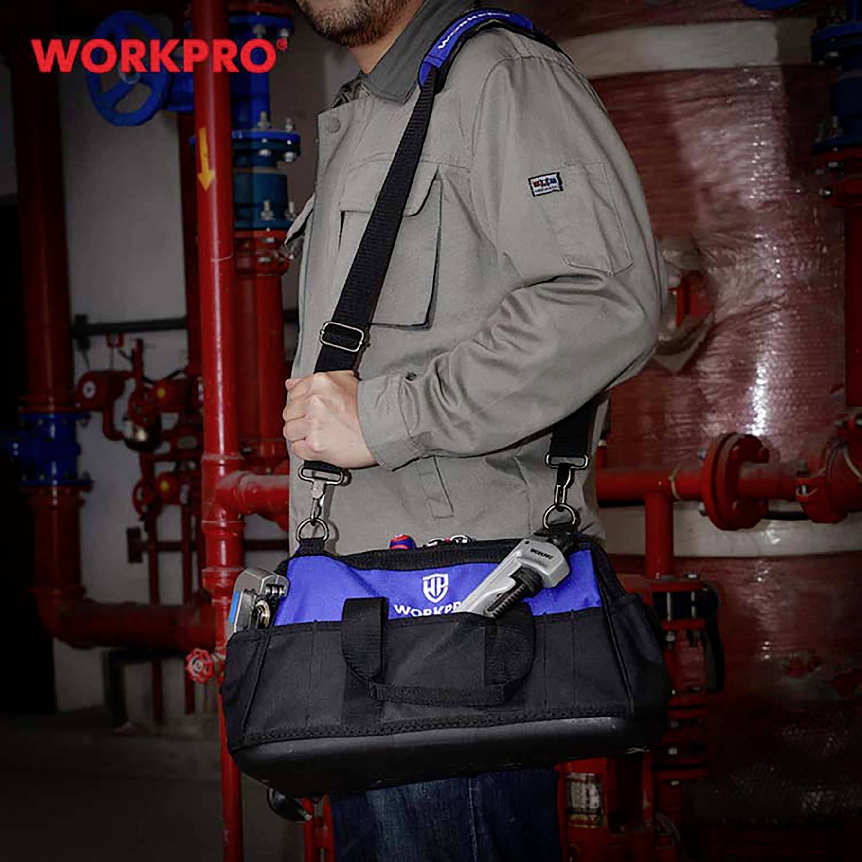 Ein Mann hält eine blaue Werkzeugtasche von Workpro, stehend vor industriell aussehenden Rohren in einem Arbeitsbereich.
