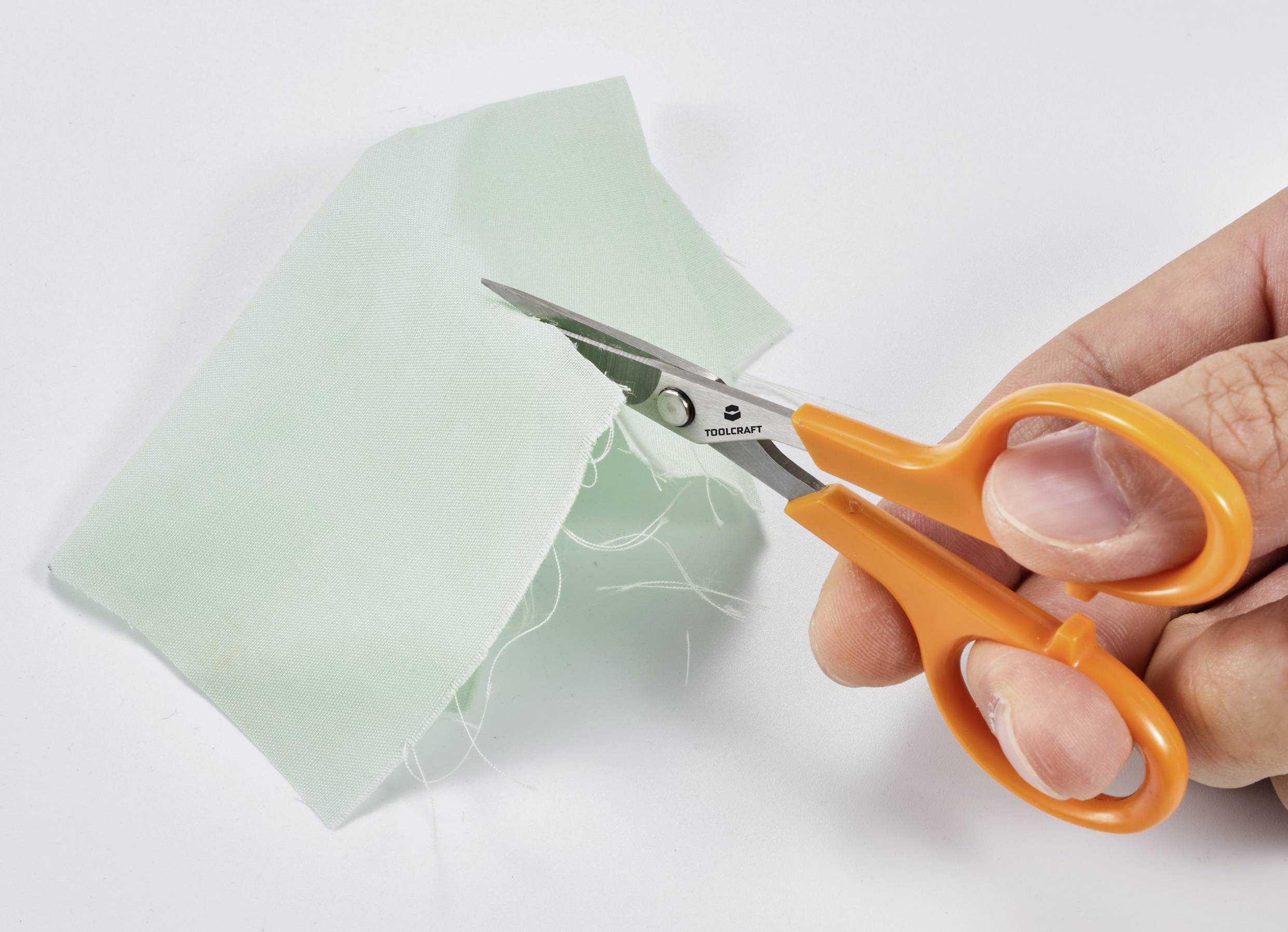 Eine Nahaufnahme einer Hand, die mit einer orangefarbenen Schere ein Stück hellgrünen Stoff schneidet.
