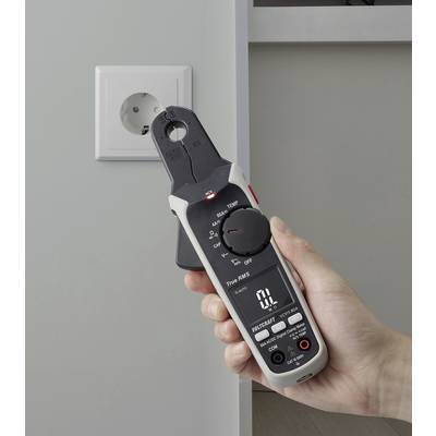 Eine Hand hält ein digitales Multimeter, das eine Steckdose misst. Das Display des Multimeters zeigt Messwerte an und deutet darauf hin, dass es gerade zur elektrischen Überprüfung verwendet wird.