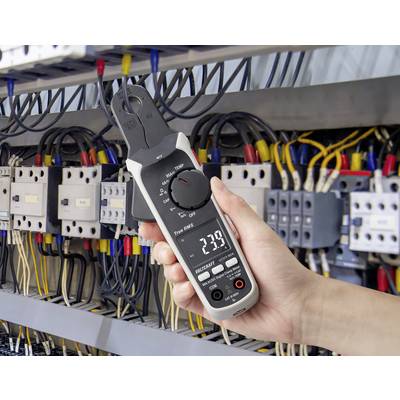 Eine Hand hält ein digitales Multimeter vor einer Elektrotafel mit Kabeln und Schaltern und zeigt eine Messung von 23,9 an.