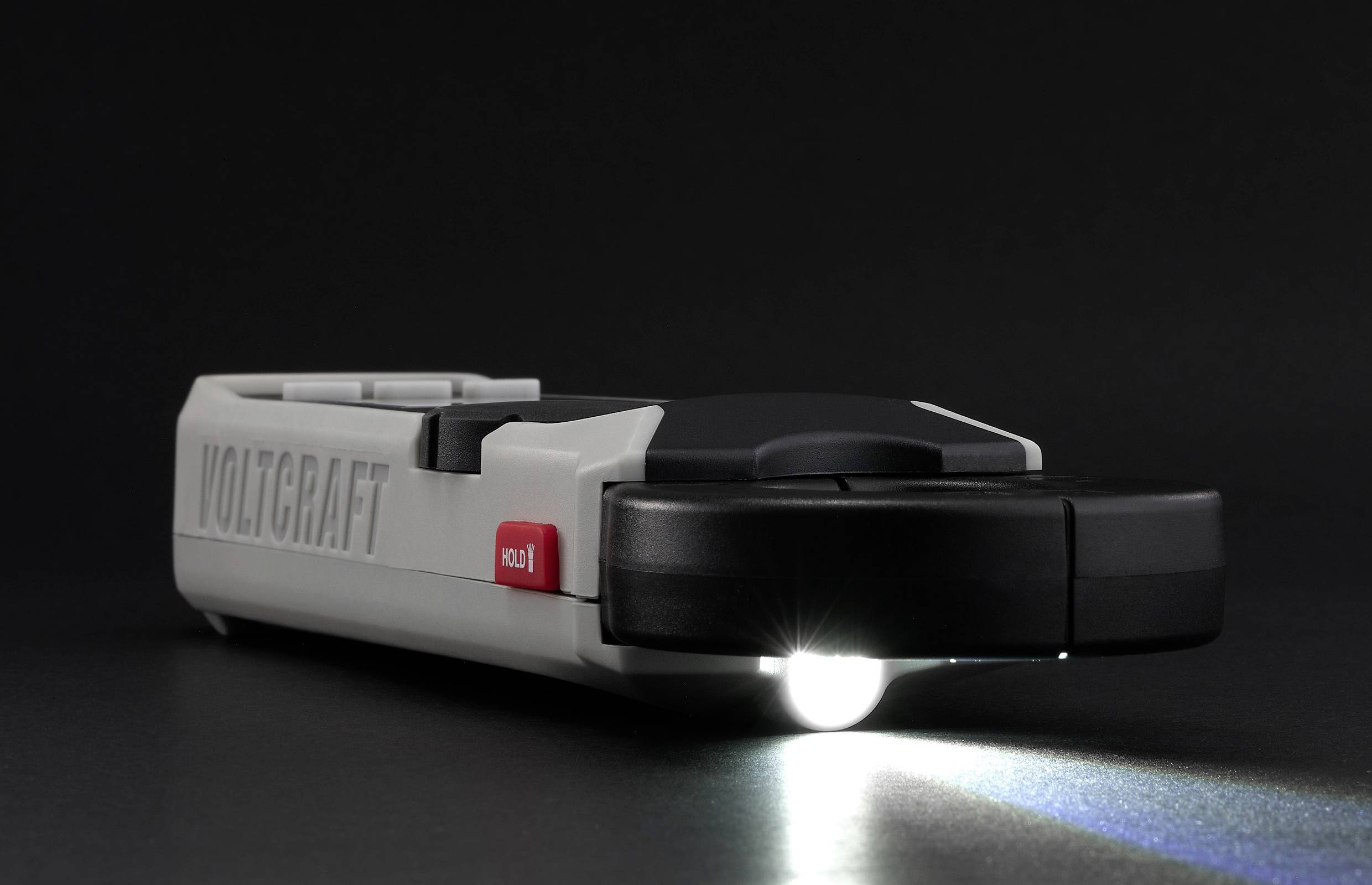 'Taschenlampe mit Voltcraft-Logo, eingeschaltet auf dunklem Hintergrund, strahlt Lichtstrahl nach rechts; rote Aus-Taste sichtbar.'