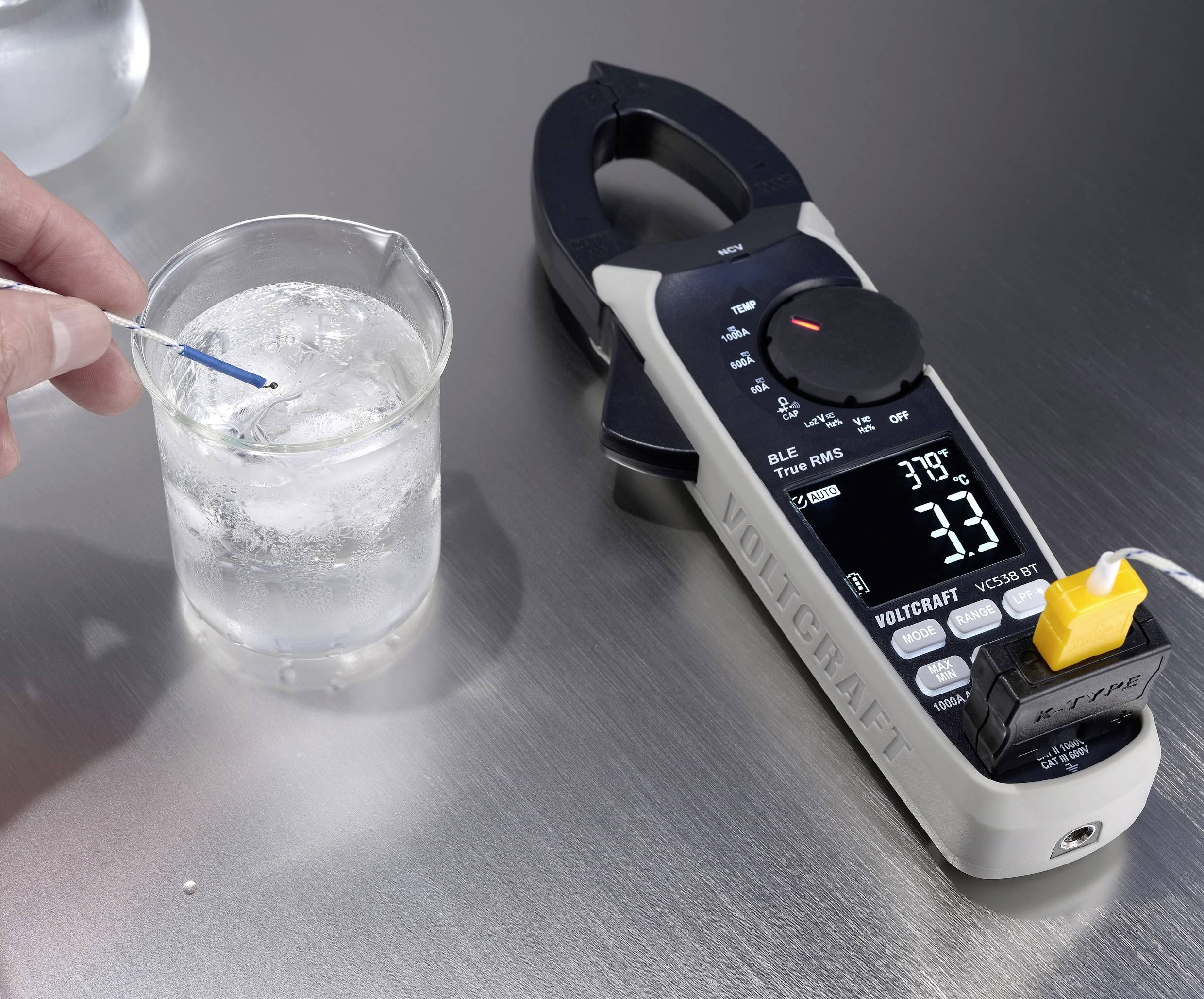 Eine Hand misst die Wassertemperatur in einem Becherglas mit einem digitalen Temperaturmessgerät, das 3,8°C anzeigt.