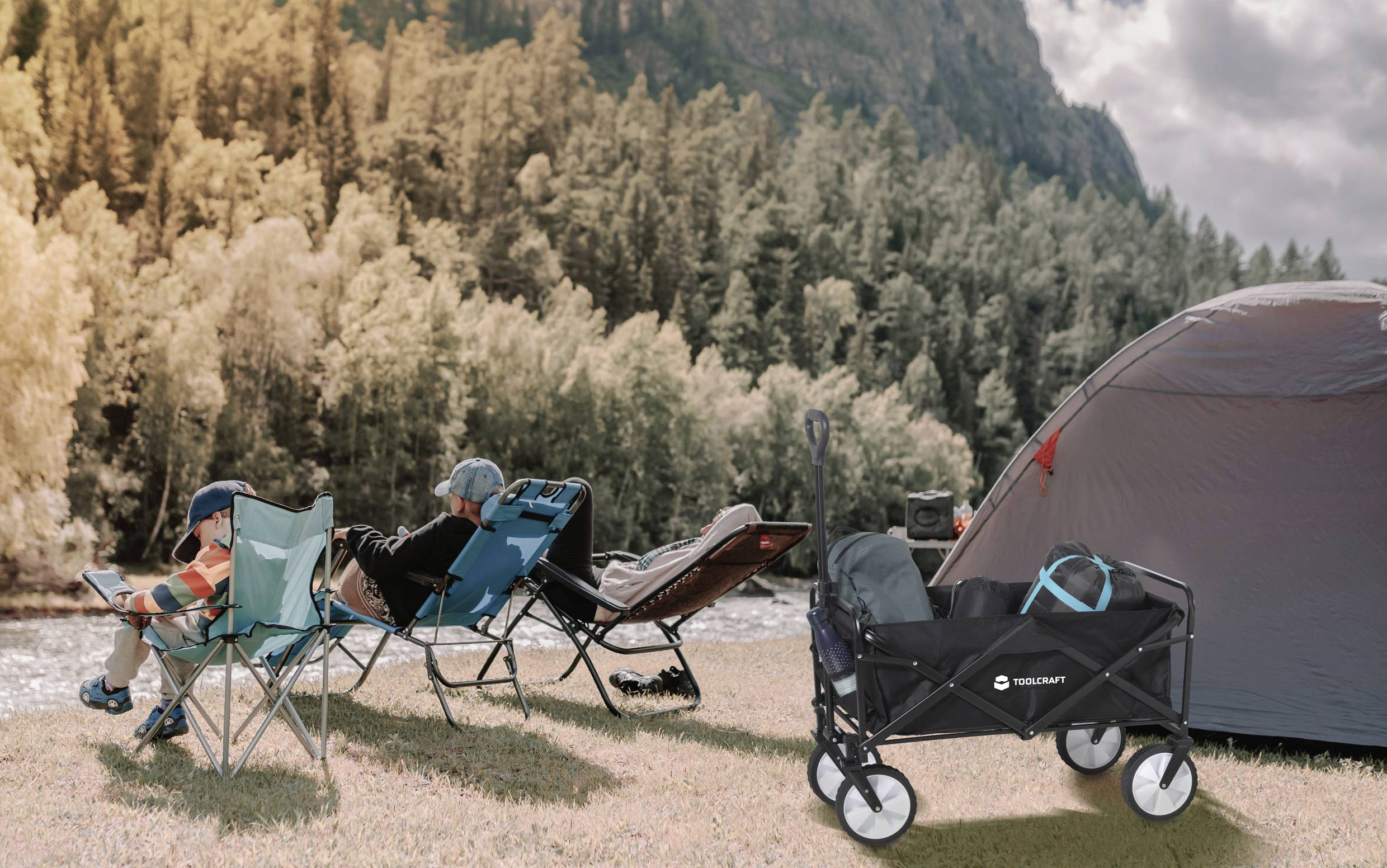 Eine Camping-Szene mit drei Personen, die auf Stühlen und einer Liege am Fluss entspannen. Ein Zelt und ein Handwagen sind im Vordergrund.