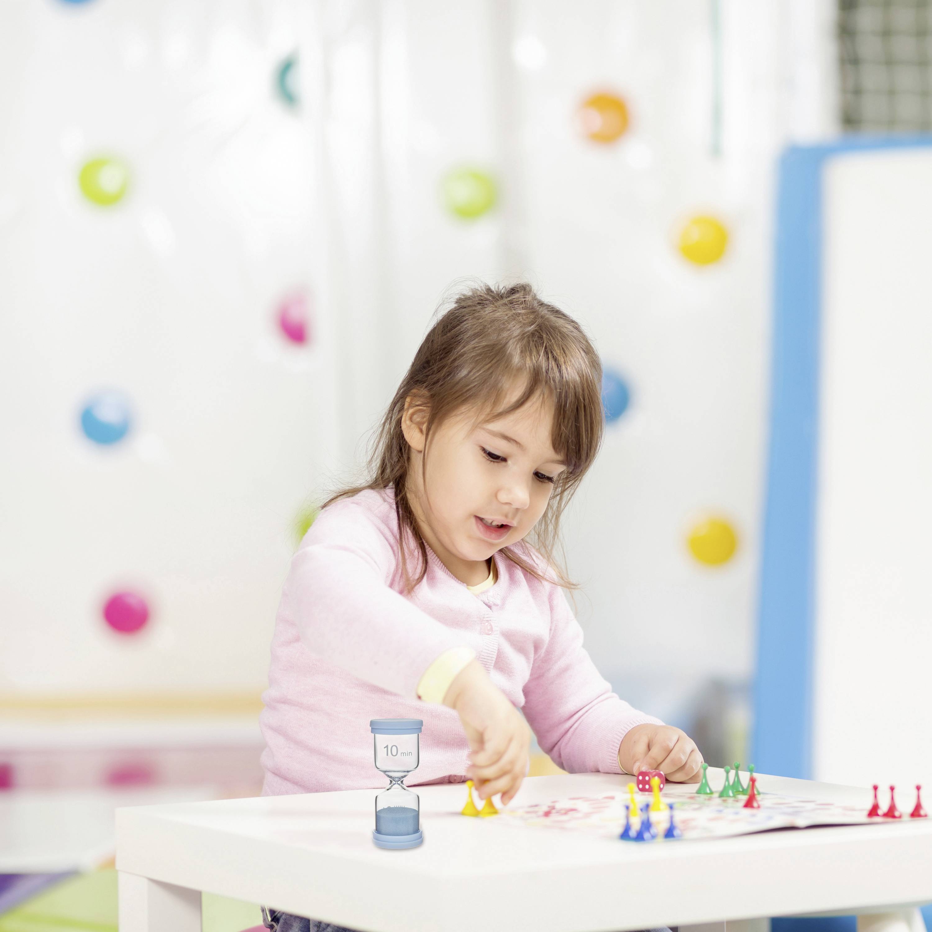 Ein kleines Kind spielt an einem Tisch, vertieft in seine Aktivität. Bunte Dekorationen im Hintergrund suggerieren eine fröhliche Umgebung.
