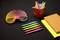 Bunte Büromaterialien auf schwarzem Hintergrund: Stifte, ein rotes Tasse mit Markern, ein Regenbogen-Slinky, zwei Notizblöcke.