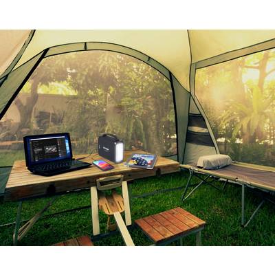 Ein Laptop, eine Powerbank und ein Tablet liegen auf einem Tisch in einem Zelt. Im Hintergrund sind Bäume. Es entsteht eine natürliche, entspannte Atmosphäre.