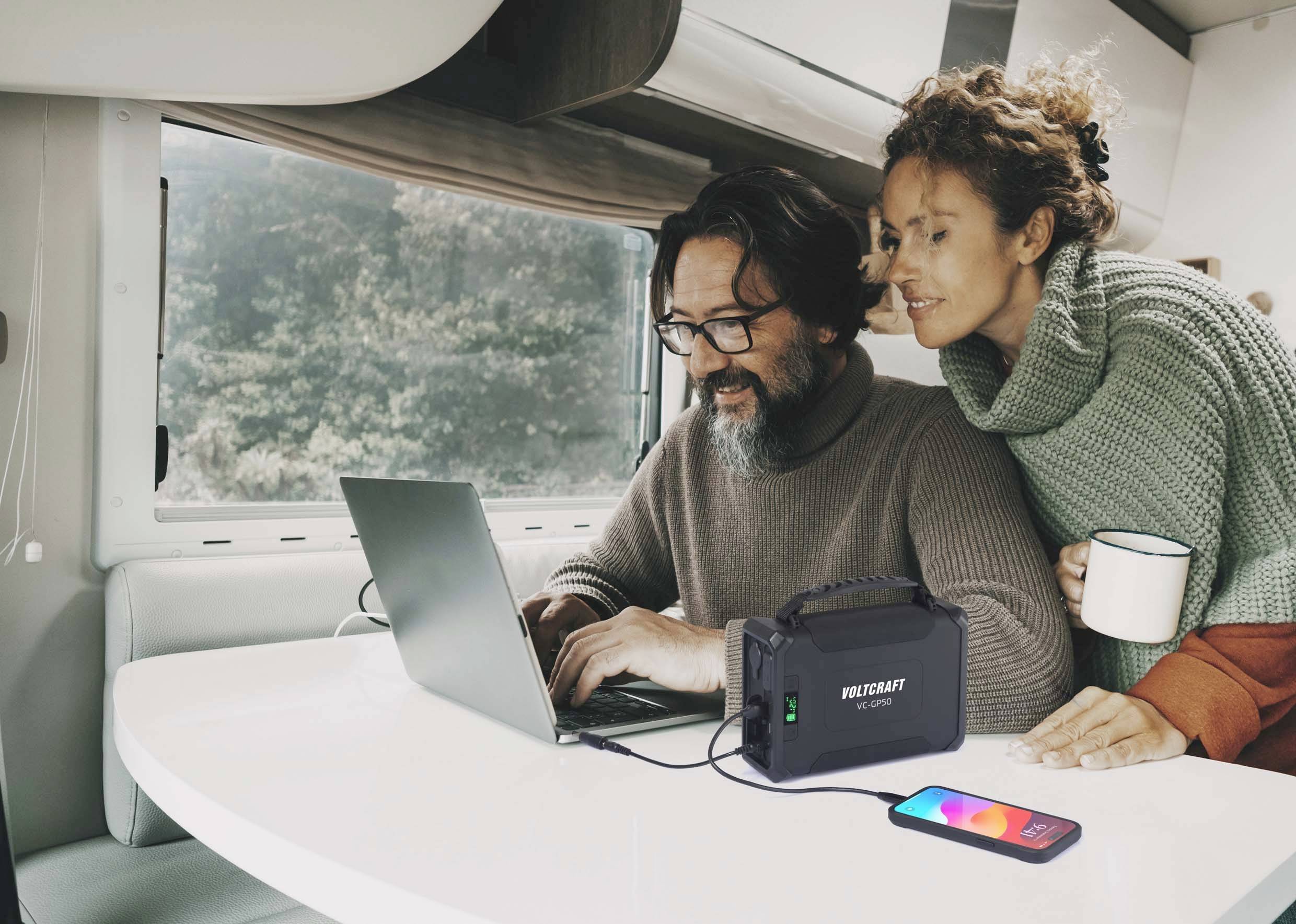 Ein Mann und eine Frau sitzen in einem Wohnmobil. Der Mann nutzt einen Laptop, der an eine tragbare Stromstation angeschlossen ist.