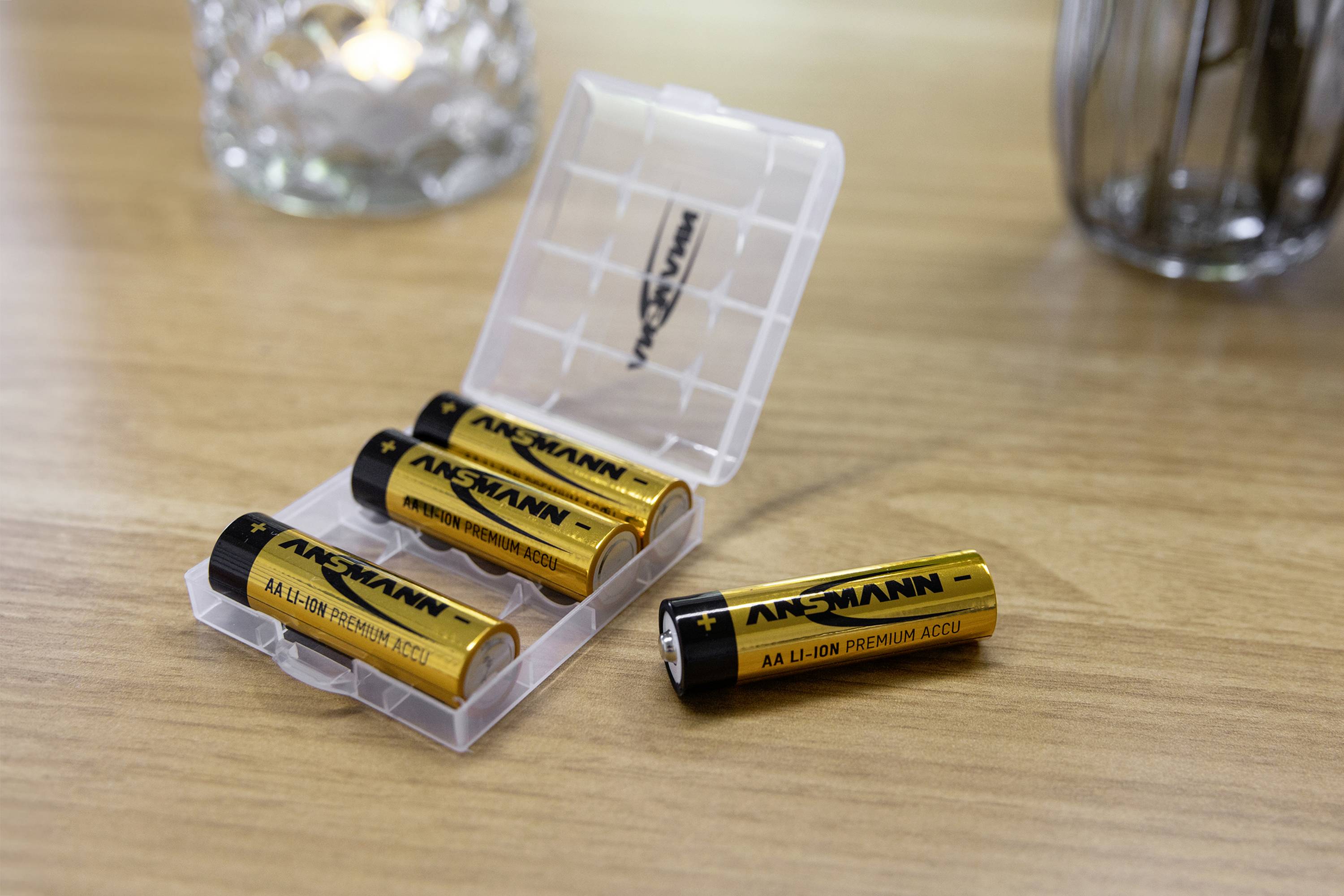 Vier AA-Lithium-Ionen-Batterien in einer offenen Kunststoffbox auf einem Holztisch. Eine Batterie liegt außerhalb der Box.