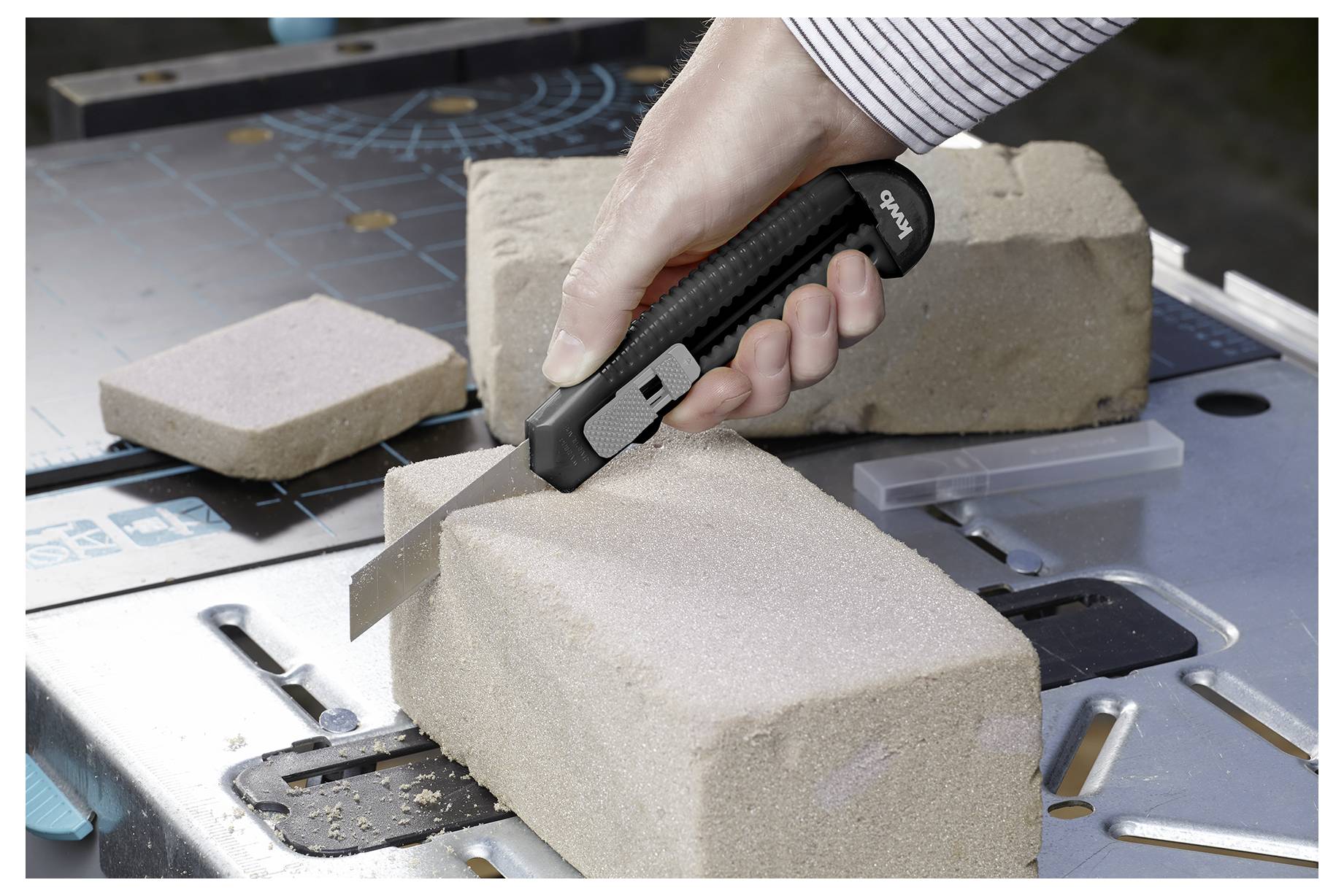 Eine Person schneidet einen Block aus weichem Material mit einem Cuttermesser auf einem Schneidebrett. Das Bild zeigt eine Nahaufnahme der Schneidbewegung.