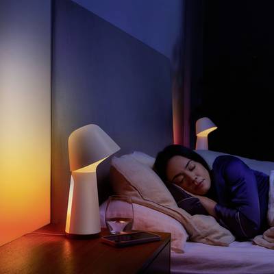 Eine Frau schläft friedlich im Bett, umgeben von sanftem Licht einer Nachttischlampe. Auf dem Nachttisch steht ein Glas Wasser.