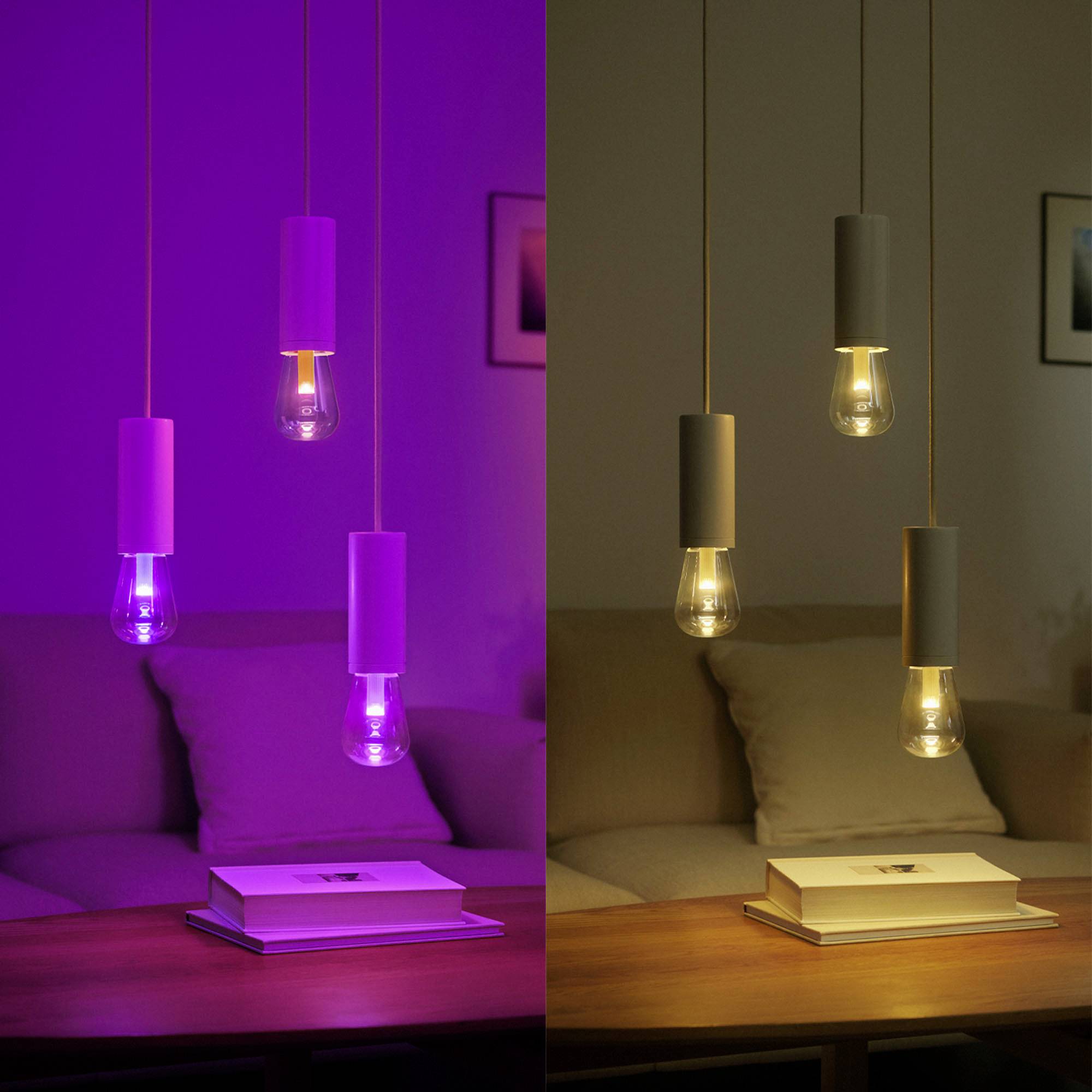 Eine Wohnzimmer-Szene mit zwei Hängelampen, die linke Lampe leuchtet lila, die rechte Lampe warmweiß. Darunter ein Tisch mit einem Buch.