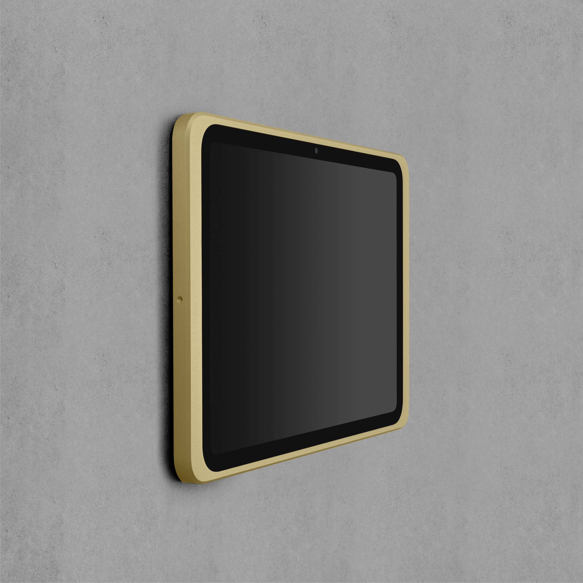 Tablet mit goldfarbenem Rahmen, an einer grauen Wand montiert. Bildschirm ist ausgeschaltet und spiegelt kein Licht.