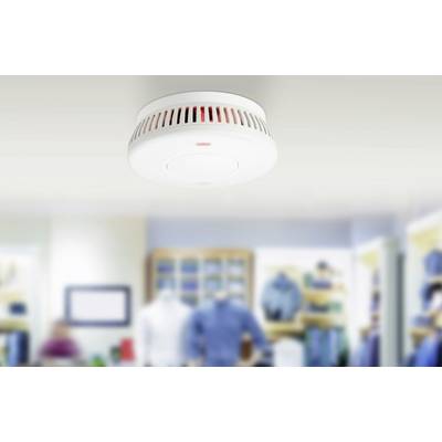 Ein Rauchmelder ist an der Decke eines modernen Geschäftsraums montiert. Im Hintergrund sind unscharf Regale mit Kleidung zu sehen.