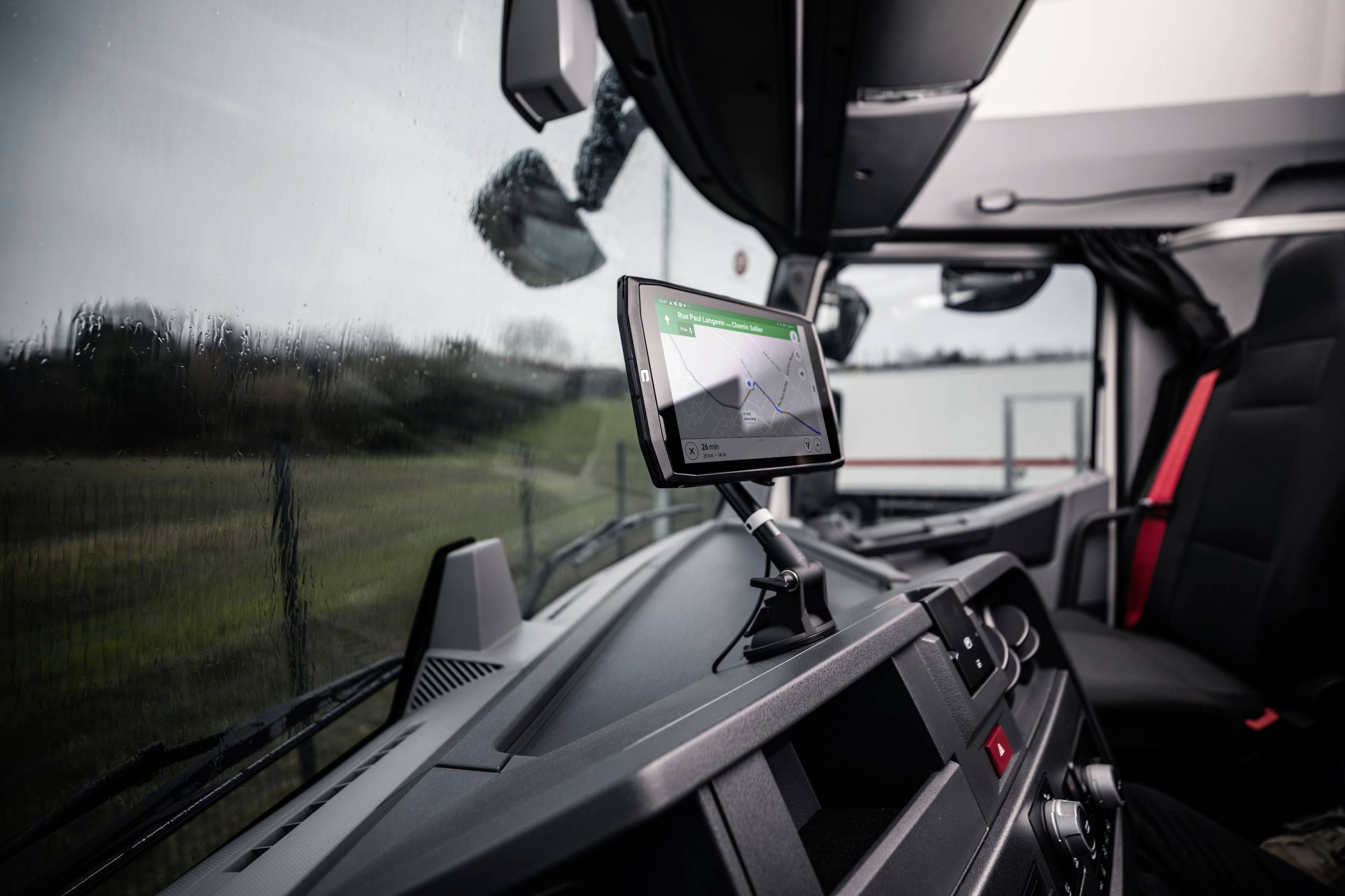 Innenansicht eines Lkw-Fahrerhauses mit einem Navigationssystem, das eine Straßenkarte anzeigt. Regentropfen auf der Windschutzscheibe.
