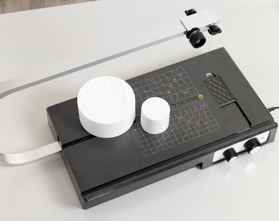Ein schwarzer Schneideplotter mit zwei weißen, zylinderförmigen Objekten unterschiedlicher Größe auf dem Messtisch.