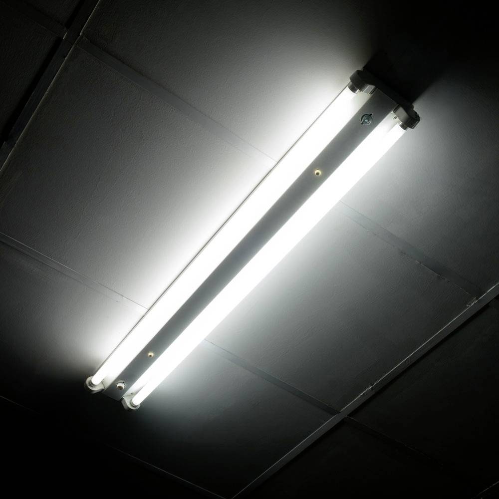 Eine leuchtende, längliche Deckenleuchte, montiert auf einer dunklen Decke, spendet helles, weißes Licht.