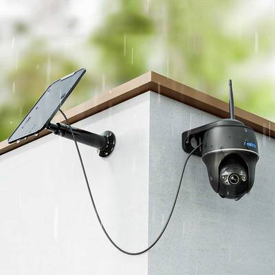 Eine Überwachungskamera mit Solarpanel ist an der Ecke eines Gebäudes montiert. Es regnet und die Kamera ist nach unten gerichtet.