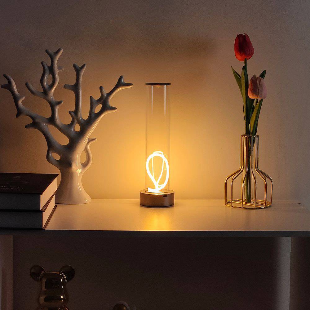 Ein stilvoller Tisch mit einer leuchtenden Lampe in der Mitte; links Bücher und rechts eine Vase mit dunkelroten und gelben Tulpen.