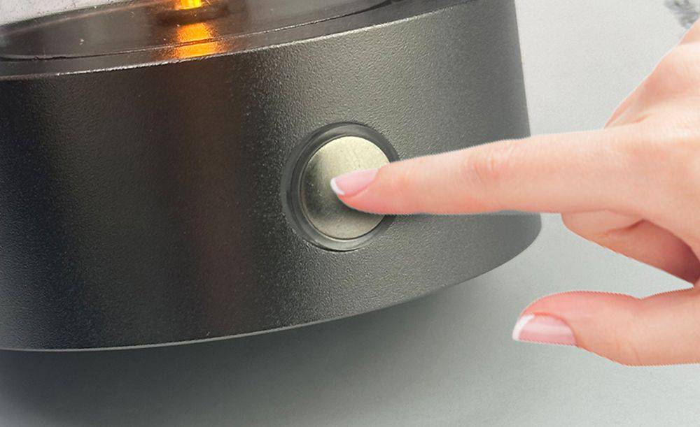 Eine Person drückt einen Knopf an einem elektrischen Gerät. Im Hintergrund leuchtet eine orangefarbene Anzeige.