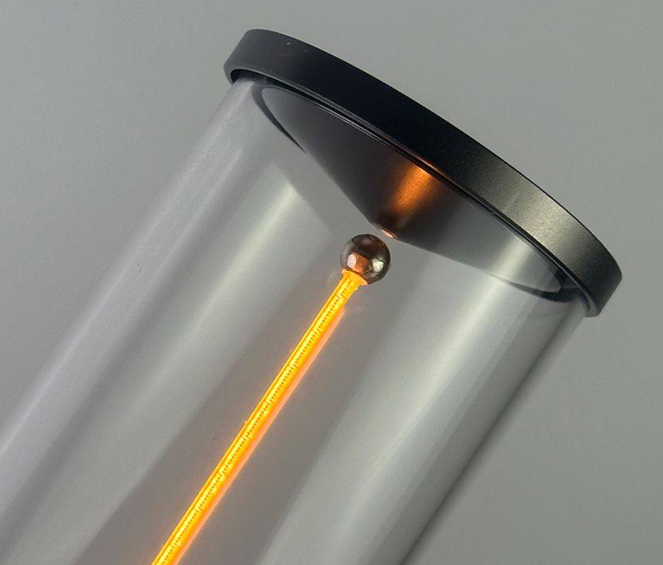 Ein durchsichtiger Zylinder mit einem leuchtend orangefarbenen Lichtstrahl in der Mitte und einem dunkelgrauen Deckel.