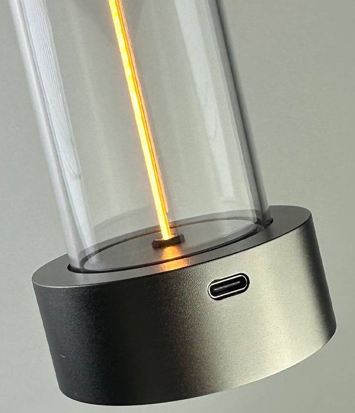 Eine Glaslampe mit zylindrischem Metallfuß. Durch den Sockel verläuft ein leuchtender oranger Faden. USB-C-Anschluss sichtbar.