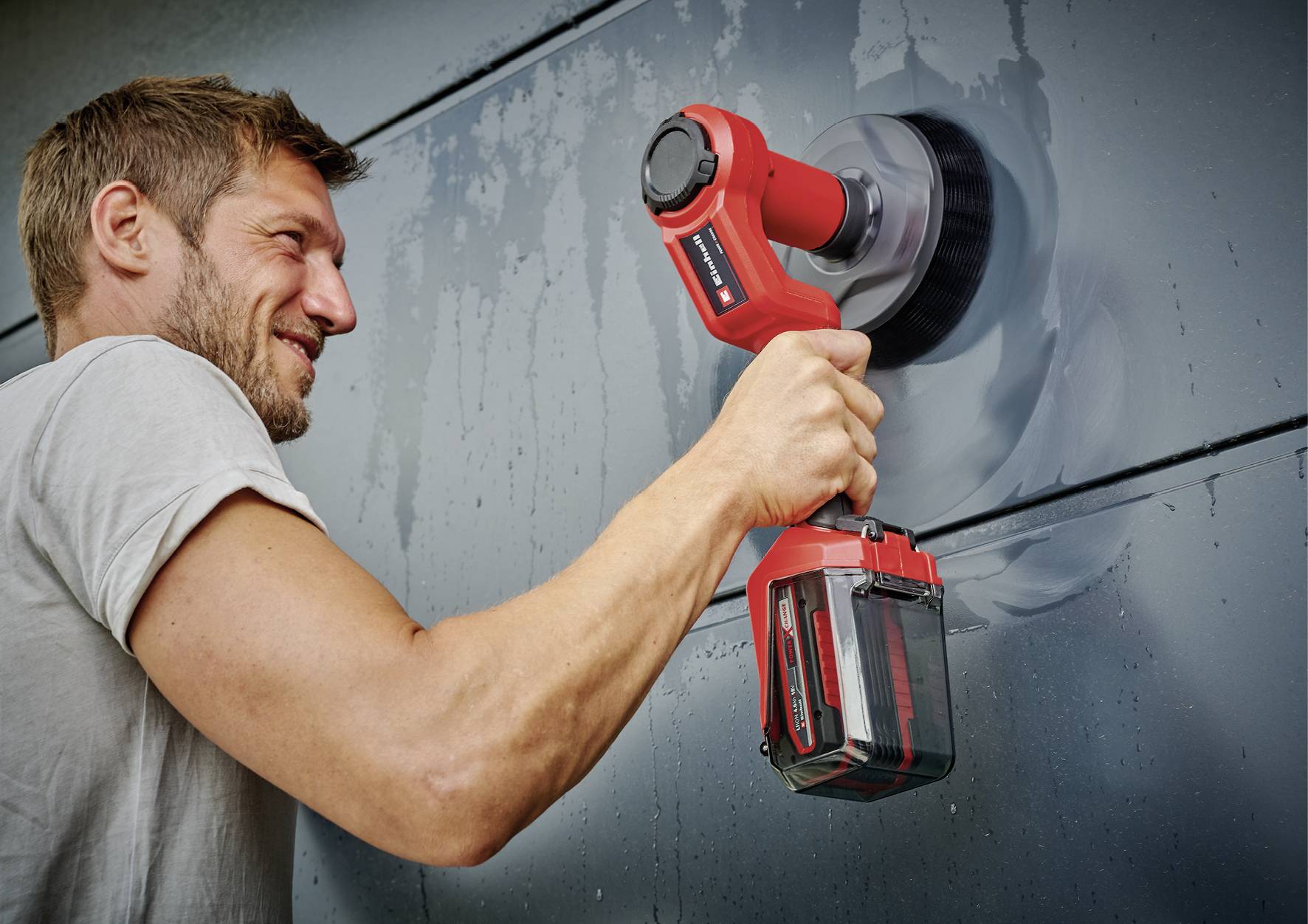 Ein Mann poliert mit einem roten Elektrowerkzeug eine Metalloberfläche. Er hält das Gerät dicht an die Oberfläche und konzentriert sich auf die Arbeit.
