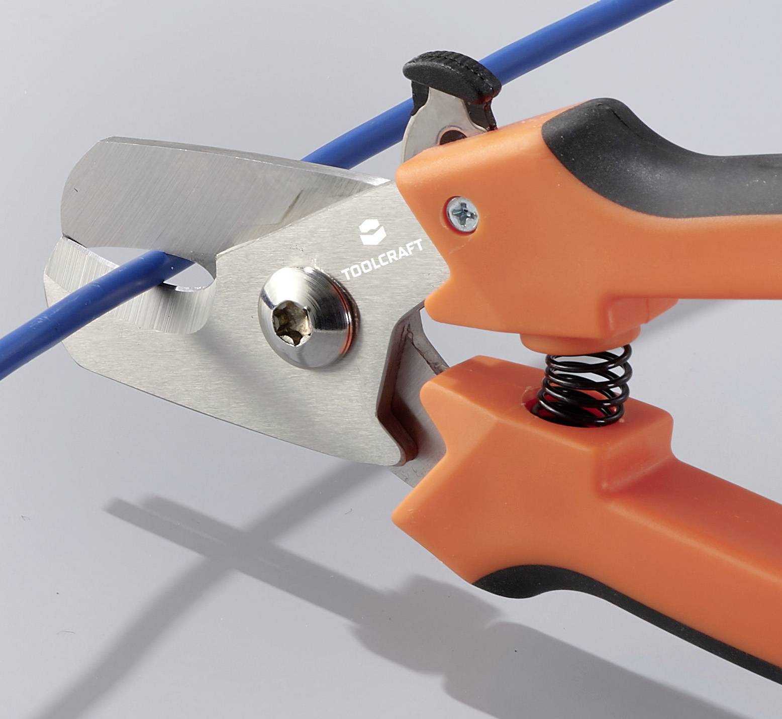 Ein Paar orangefarbene Kabelschneider schneidet ein blaues Kabel. Im Hintergrund ist eine graue Oberfläche sichtbar.