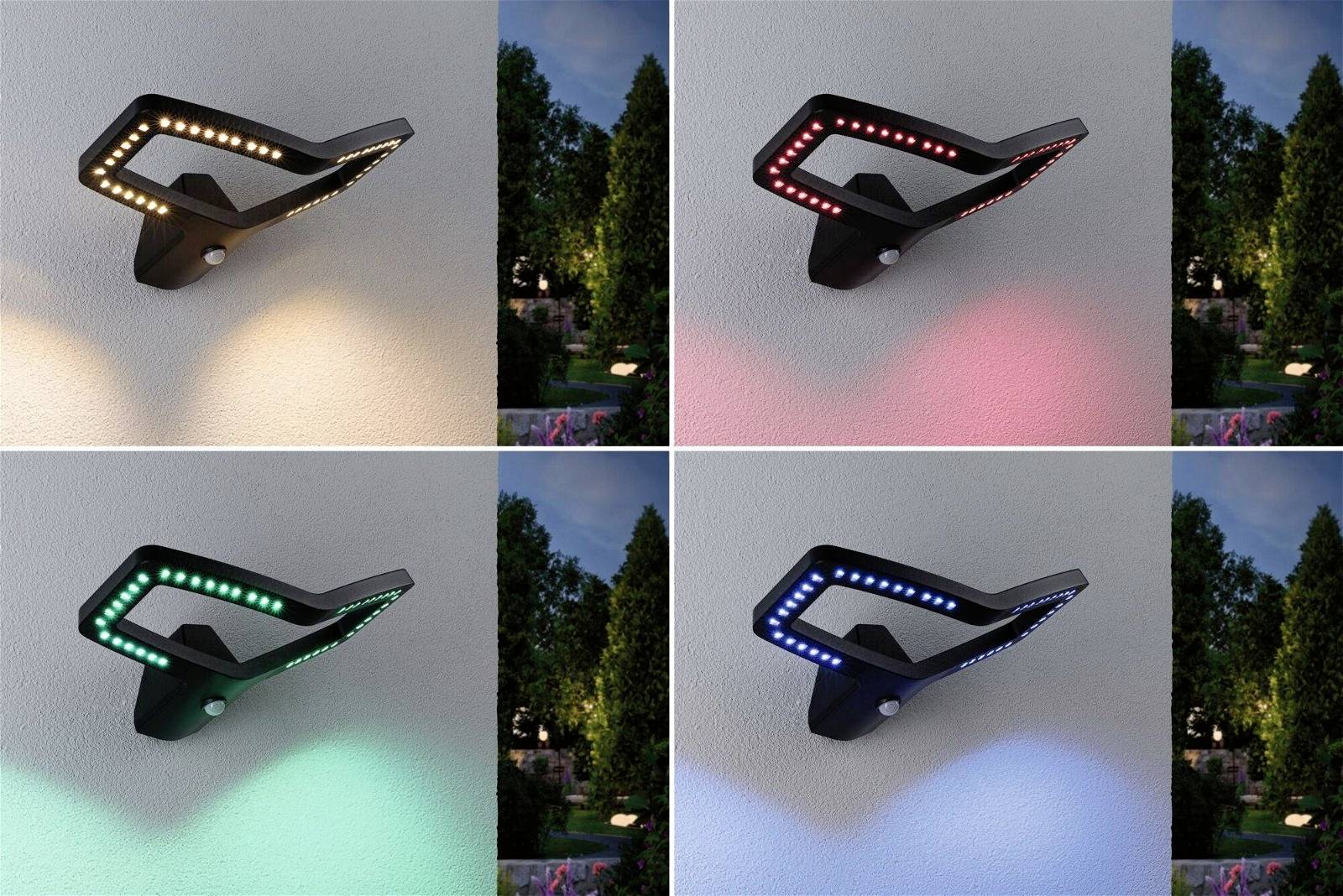 Vier Wandlampen leuchten in verschiedenen Farben: weiß, rot, grün und blau. Sie beleuchten eine Wand neben einem Garten.