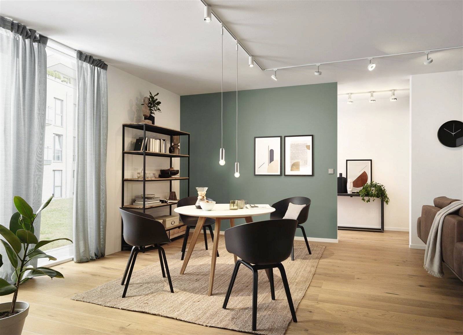 Ein modern eingerichtetes Wohnzimmer mit Holzboden, rundem Tisch und vier schwarzen Stühlen, dekoriert mit Pflanzen und Wandbildern.