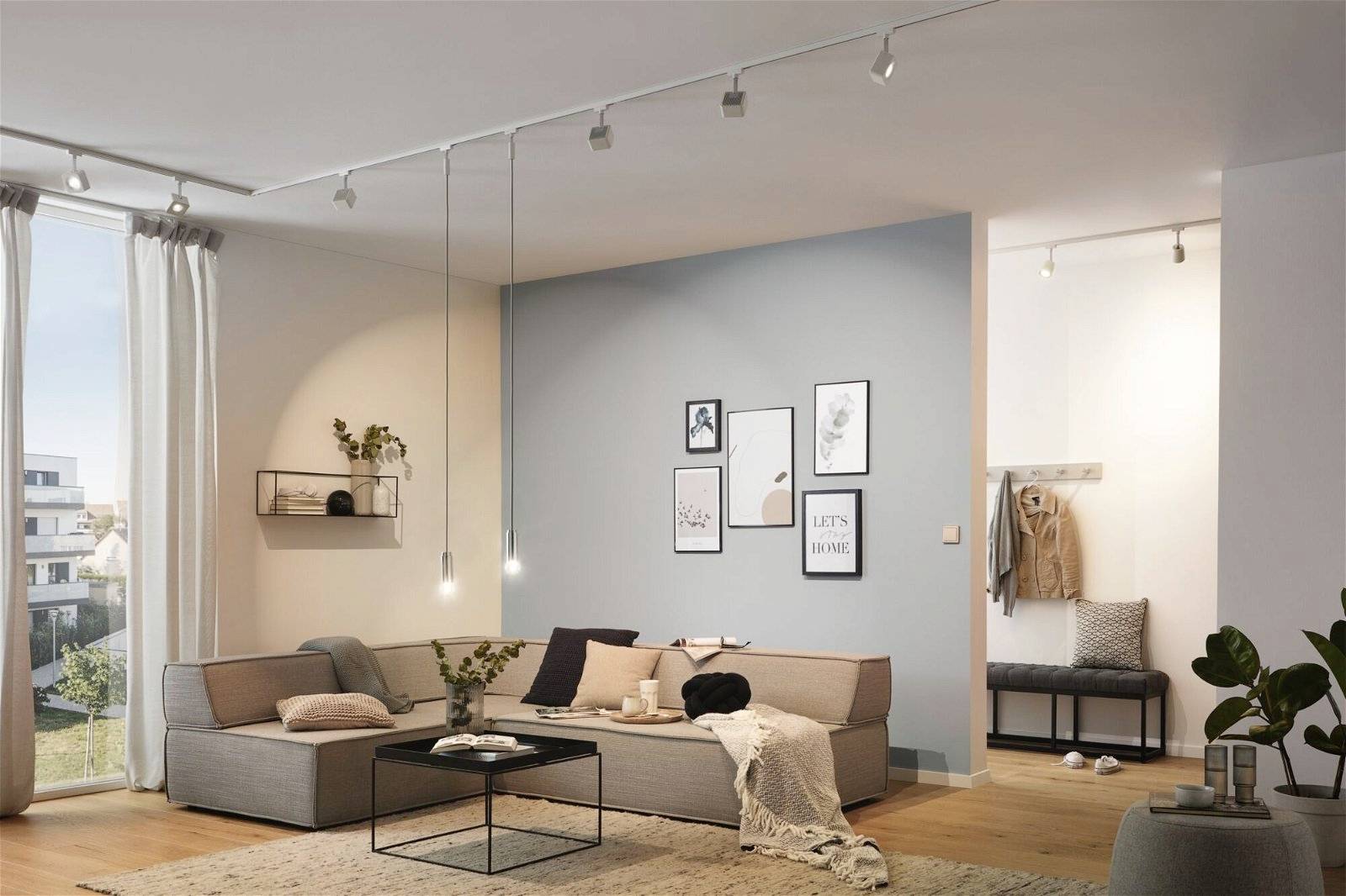 Gemütliches Wohnzimmer mit Ecksofa, Couchtisch und dekorativen Bildern an der Wand. Helle, moderne Einrichtung mit hängenden Leuchten.