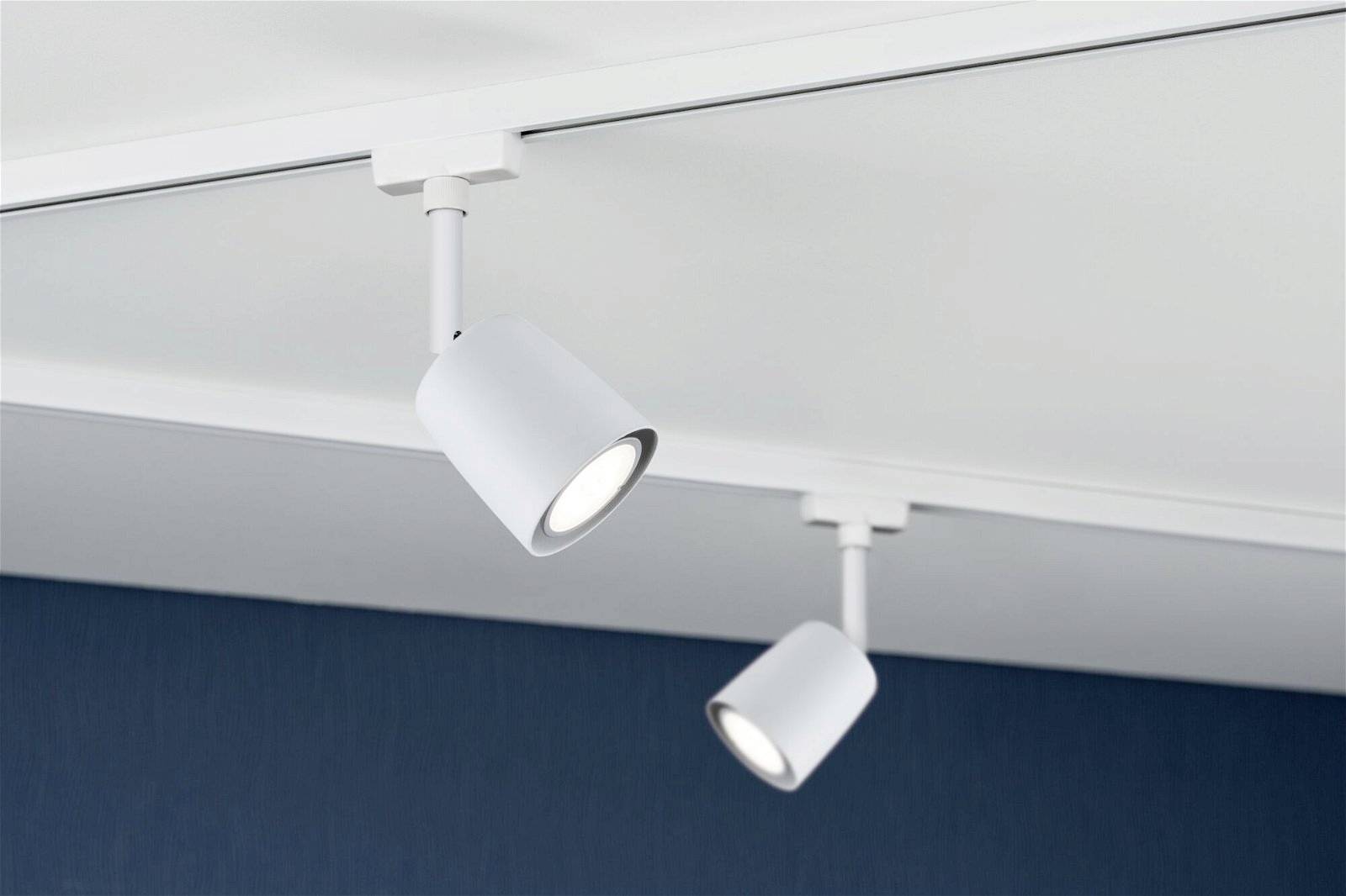 Zwei weiße Deckenstrahler an einer Schiene, die nach unten leuchten. Hintergrund ist dunkelblau.