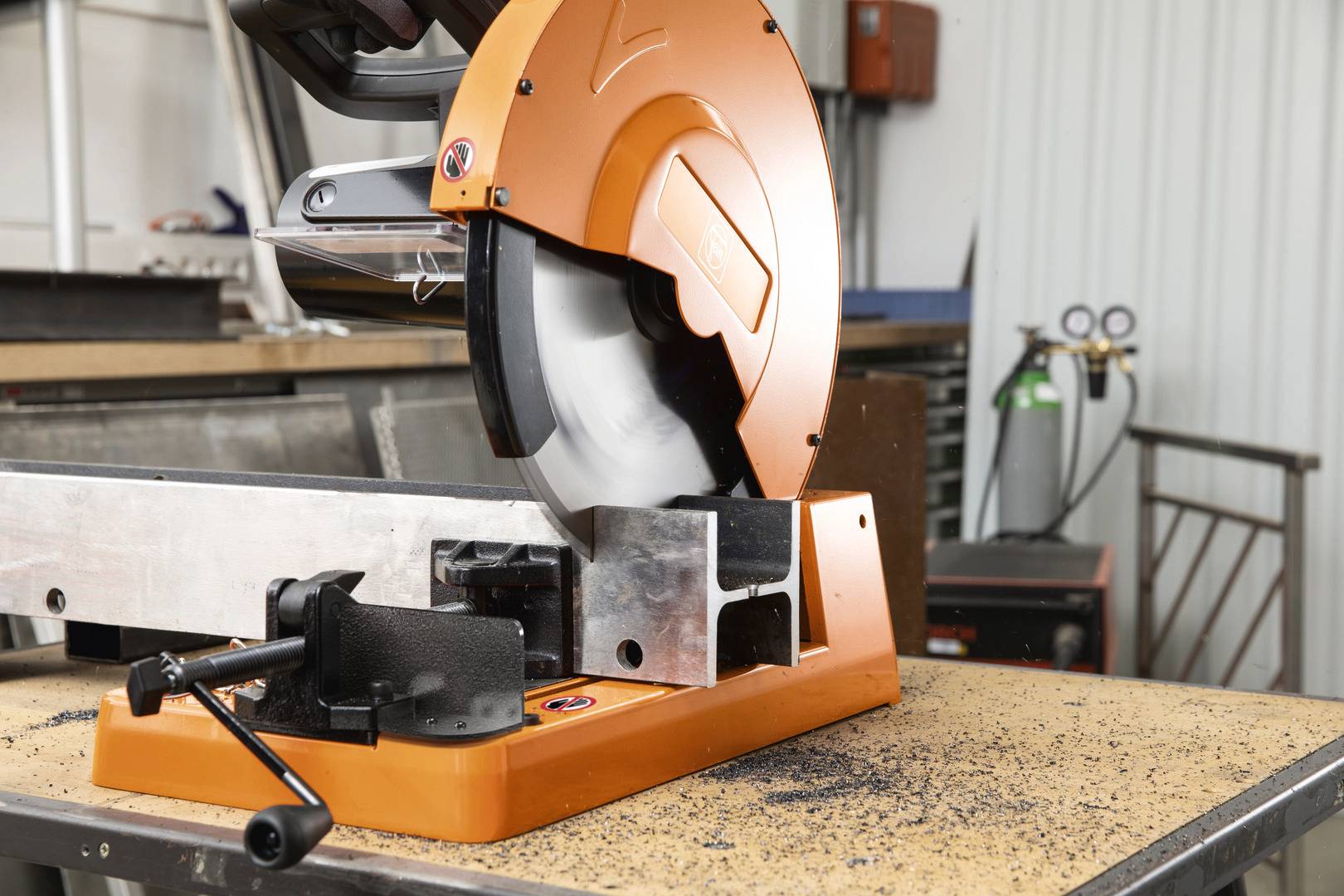 'Metallsäge in Werkstatt, schneidet Aluminiumrohr auf Werkbank. Sägemehl und Werkzeuge verstreut. Industrielle Umgebung.'