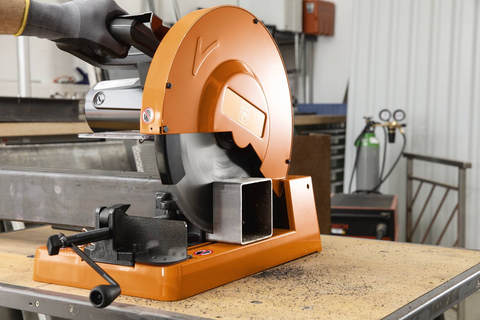 'Metallbearbeitung: Eine Kreissäge schneidet ein Metallrohr auf einem Tisch in einer Werkstatt. Schutzkleidung wird getragen.'