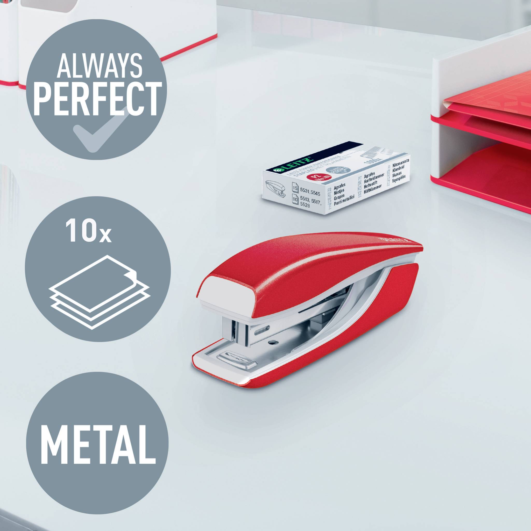 Ein roter Metallhefter liegt auf einem Schreibtisch mit Heftklammern daneben. Werbung betont Haltbarkeit: 'Always perfect', 'Metal', kapazität '10x'.