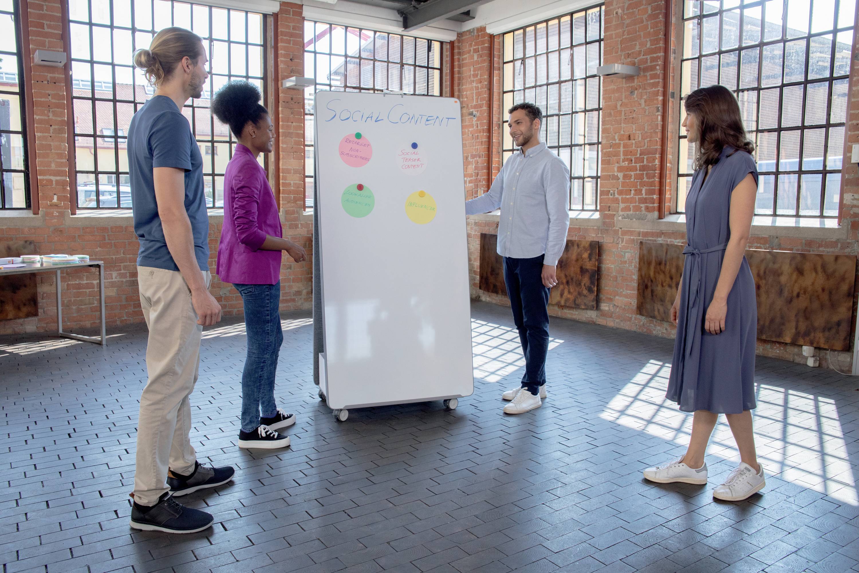 Vier Personen stehen in einem sonnigen Raum um ein beschriftetes Whiteboard mit farbigen Kreisen und diskutieren.