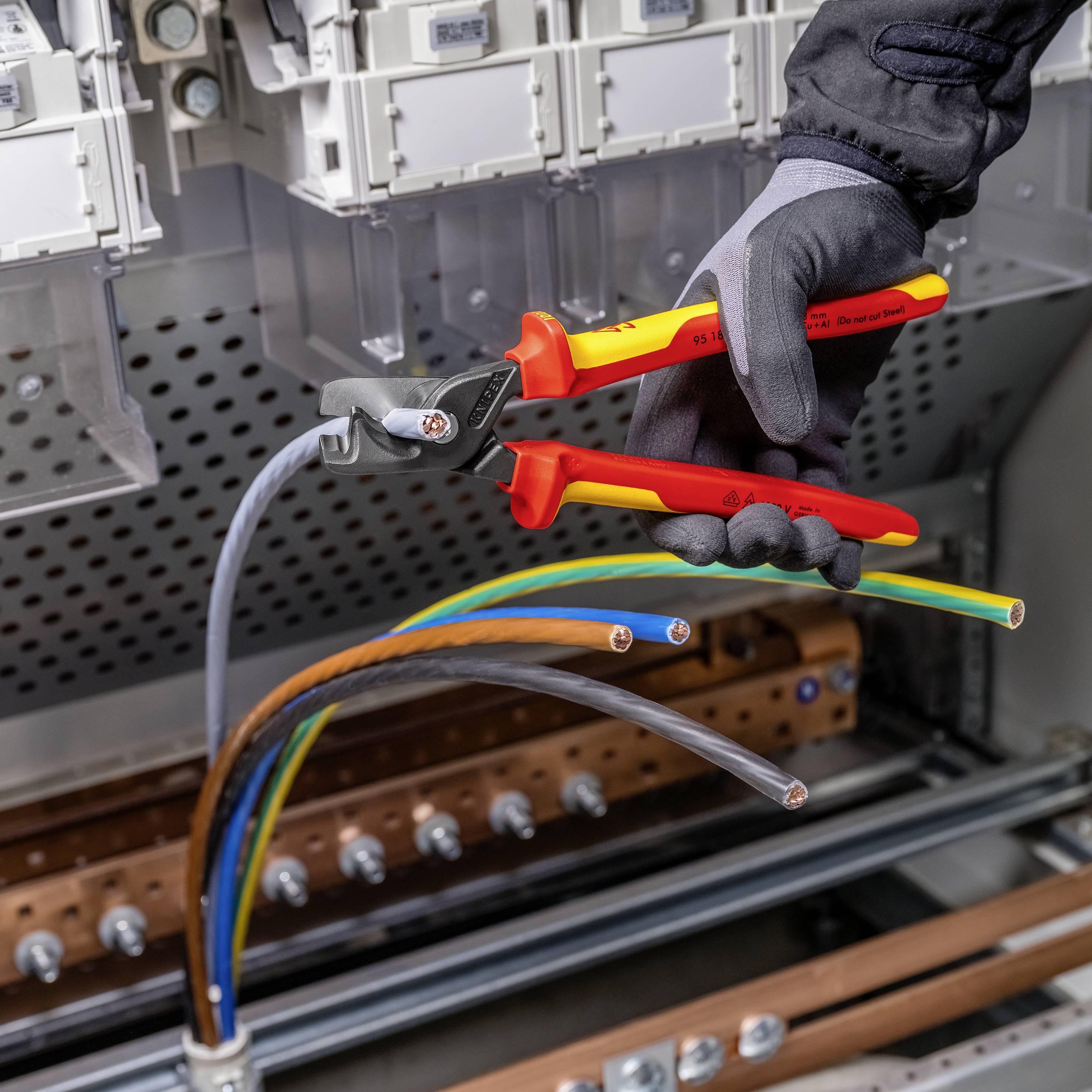 Eine Person in Schutzhandschuhen verwendet isolierte Zangen, um Kabel in einem Schaltschrank zu durchtrennen.