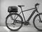 Ein schwarzes E-Bike mit Gepäckträger und montierter Tasche auf grauem Hintergrund.