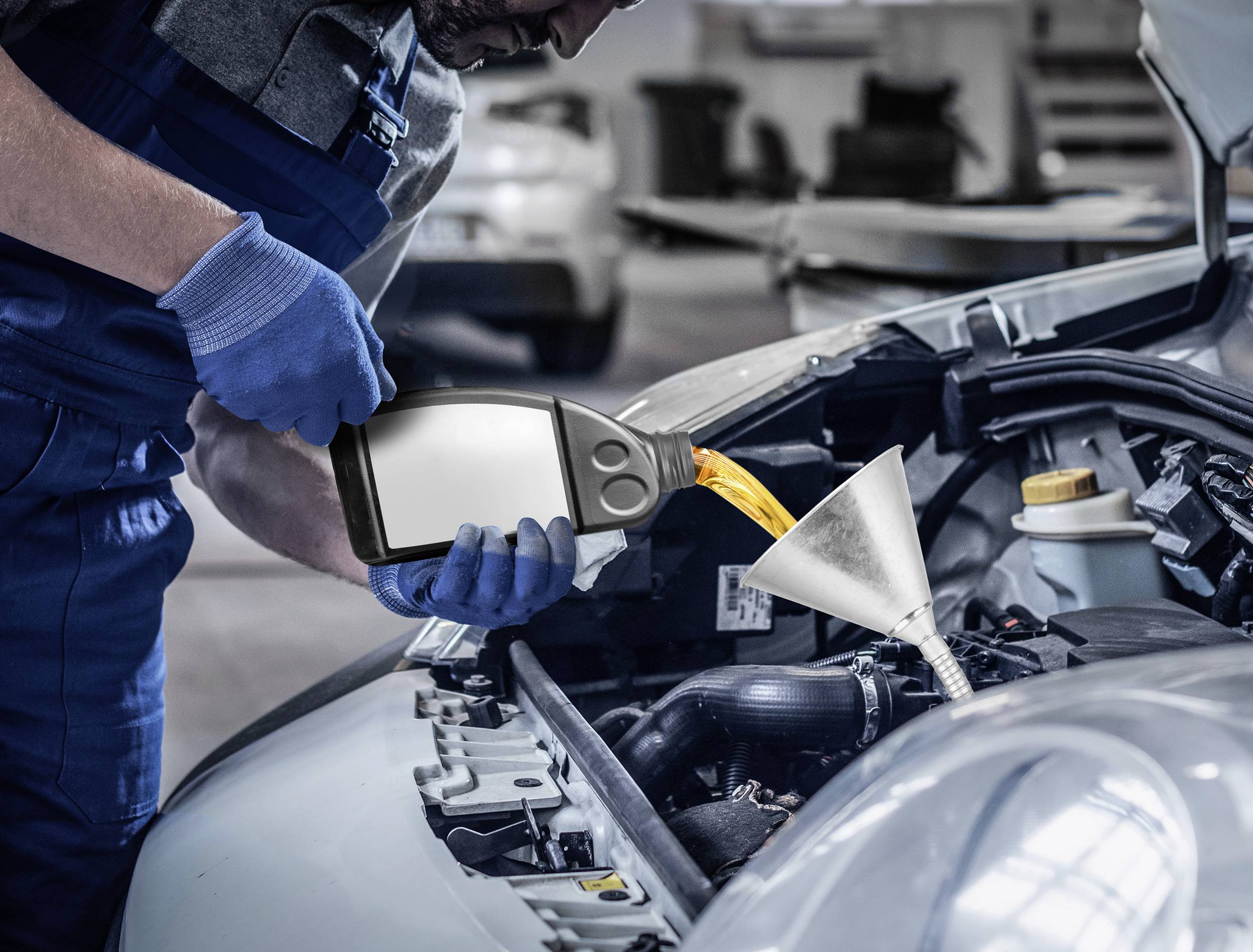 Ein Mechaniker trägt blaue Handschuhe und füllt Öl durch einen Trichter in den geöffneten Motor eines Autos in einer Werkstatt.