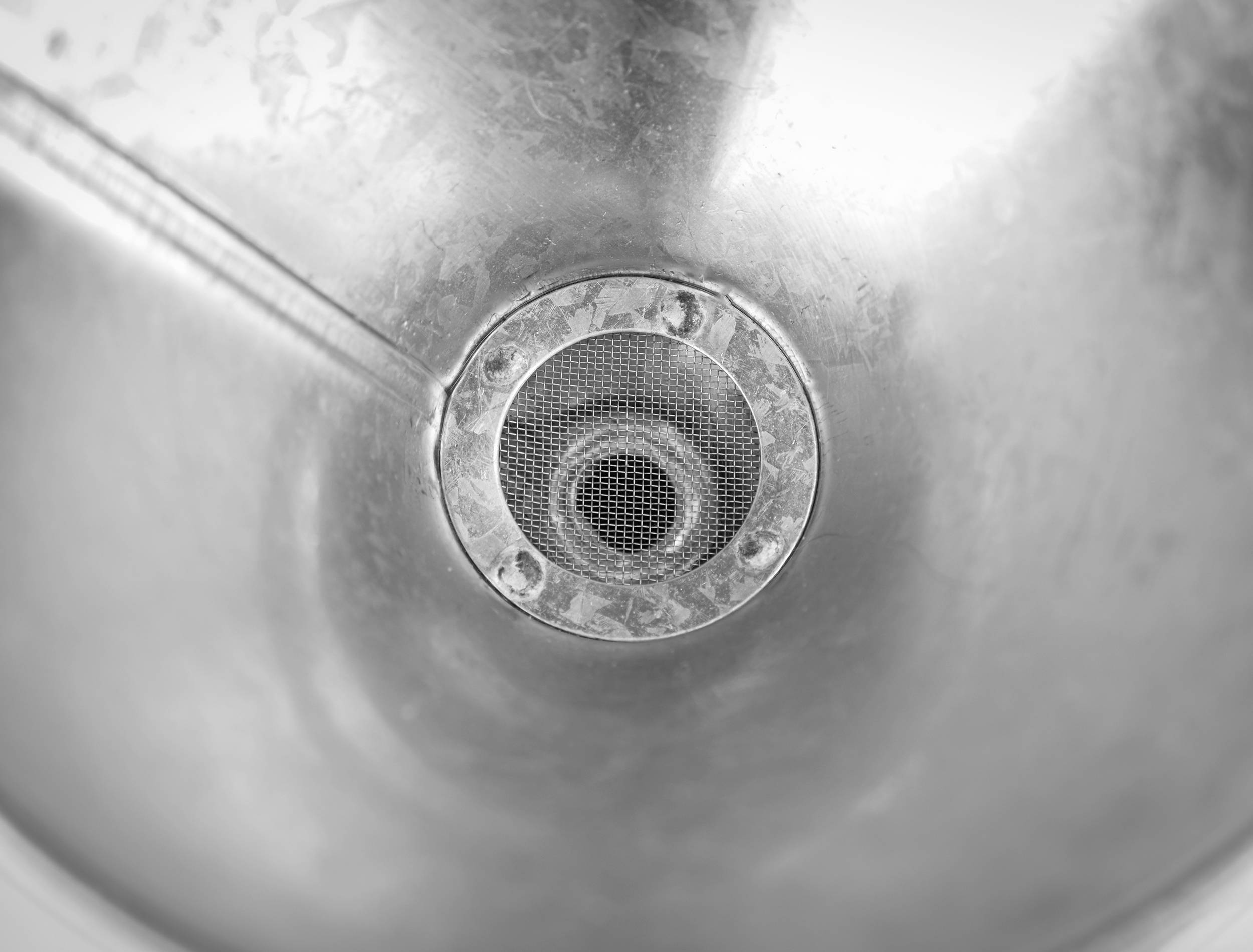 Ein verrosteter Abfluss in einem metallischen Waschbecken. Die Oberfläche ist leicht matt und zeigt Gebrauchsspuren.