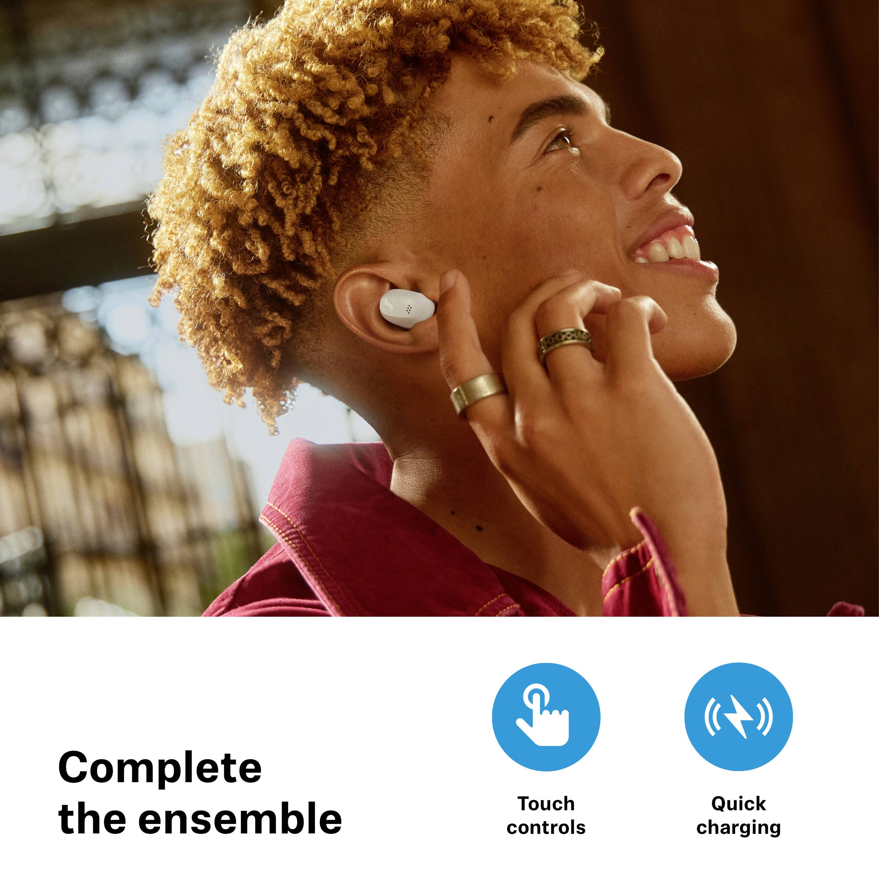 Eine Person hört Musik mit kabellosen Ohrhörern. Text unten: 'Complete the ensemble'. Symbole: 'Berührungssteuerung', 'Schnellladung'.